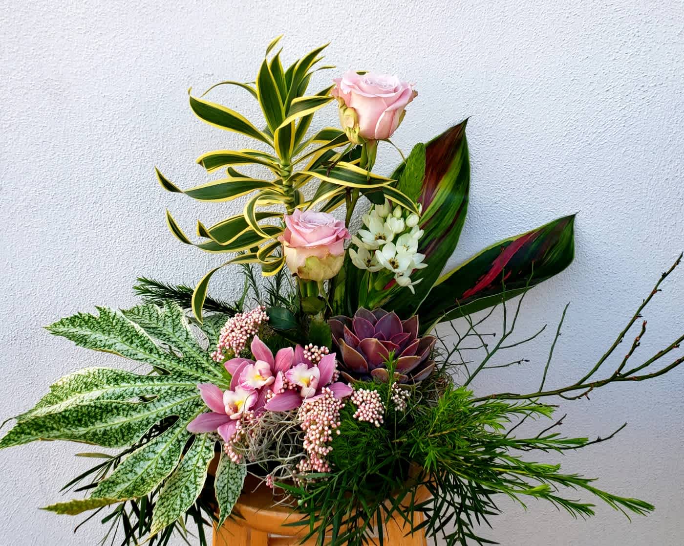 Mixed floral arrangement with pink roses, orchids, and succulents in a container