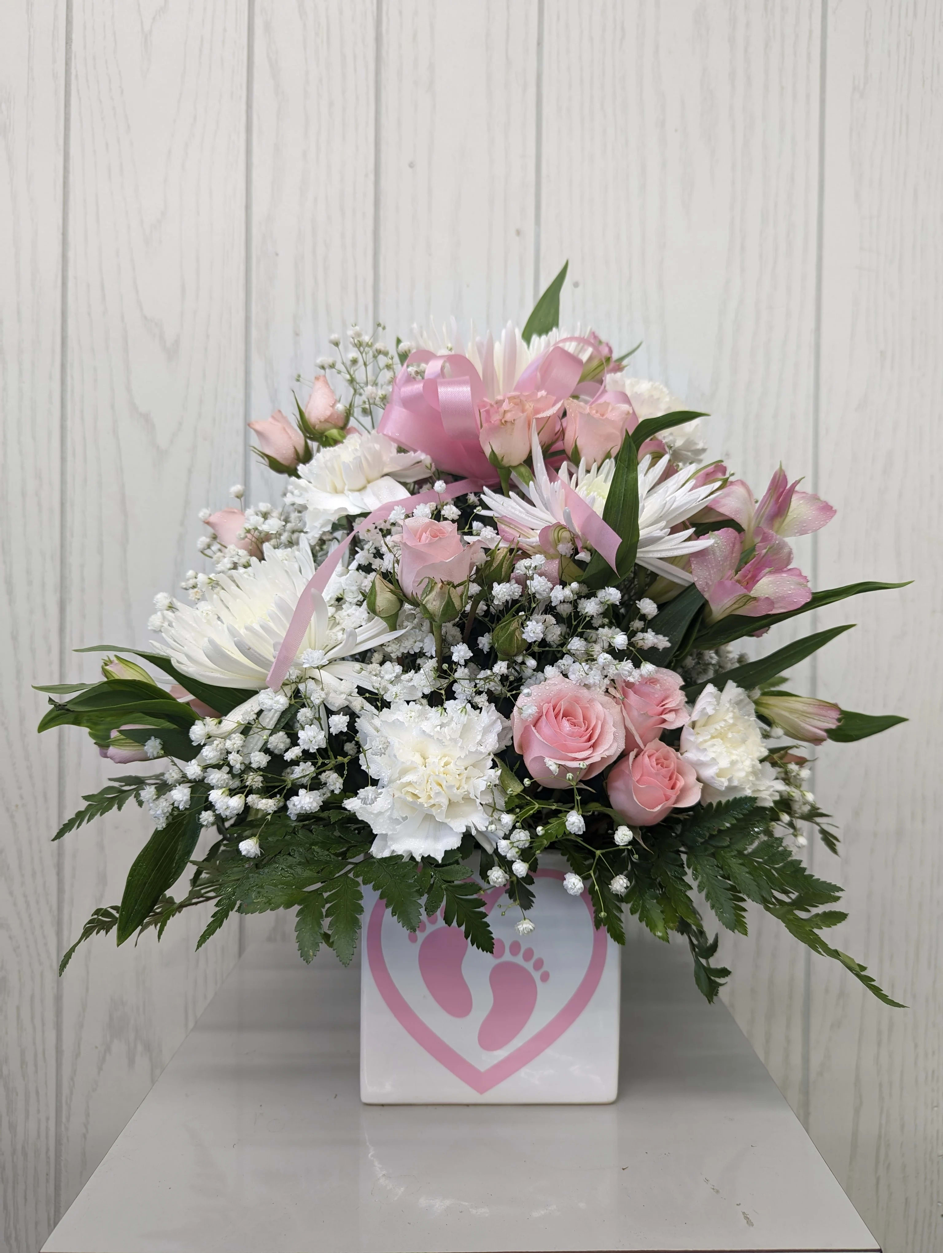 Pink and white floral arrangement in a white box with a pink footprint design