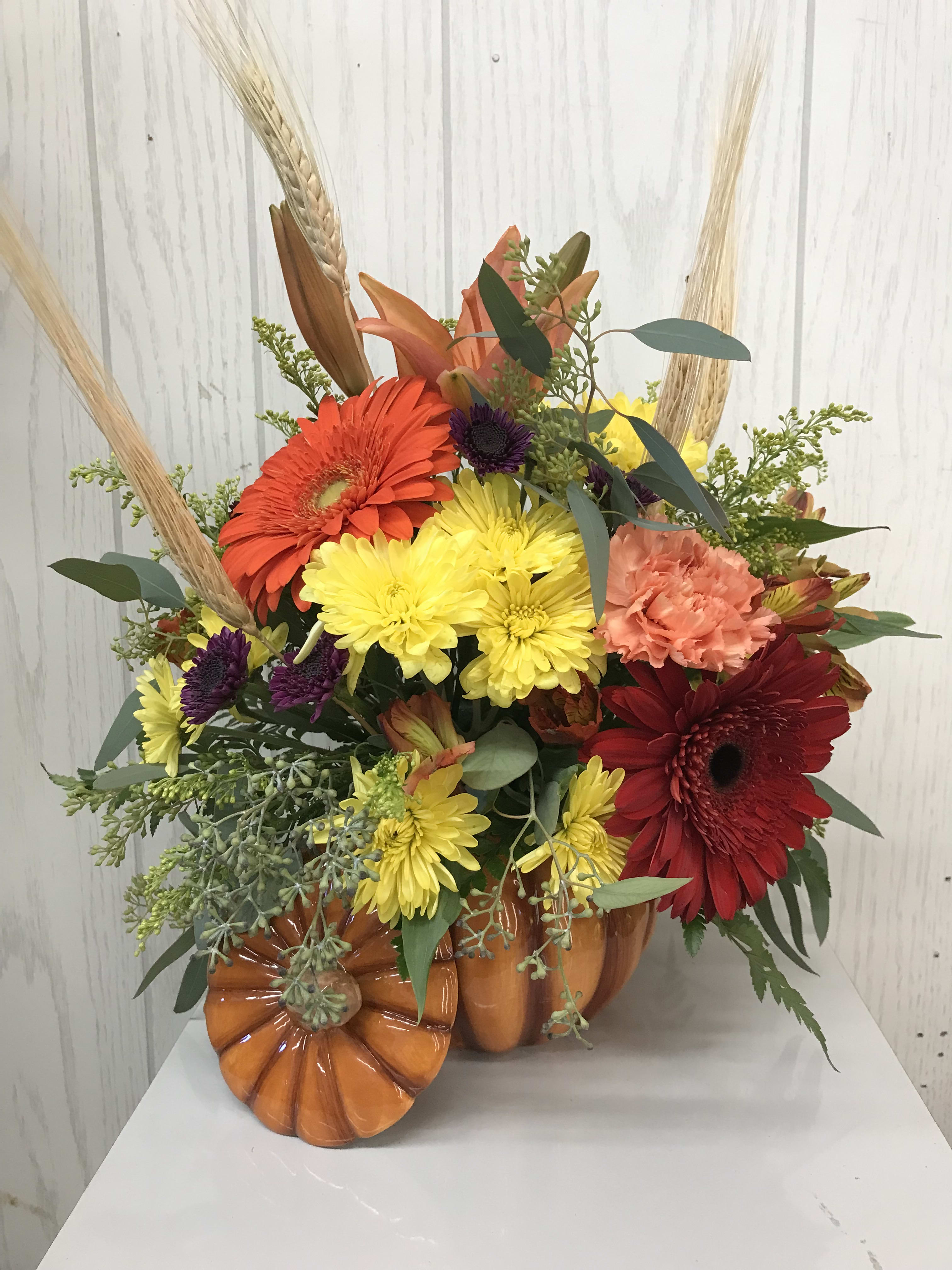 Autumn floral arrangement in a pumpkin-shaped container with bright mixed blooms