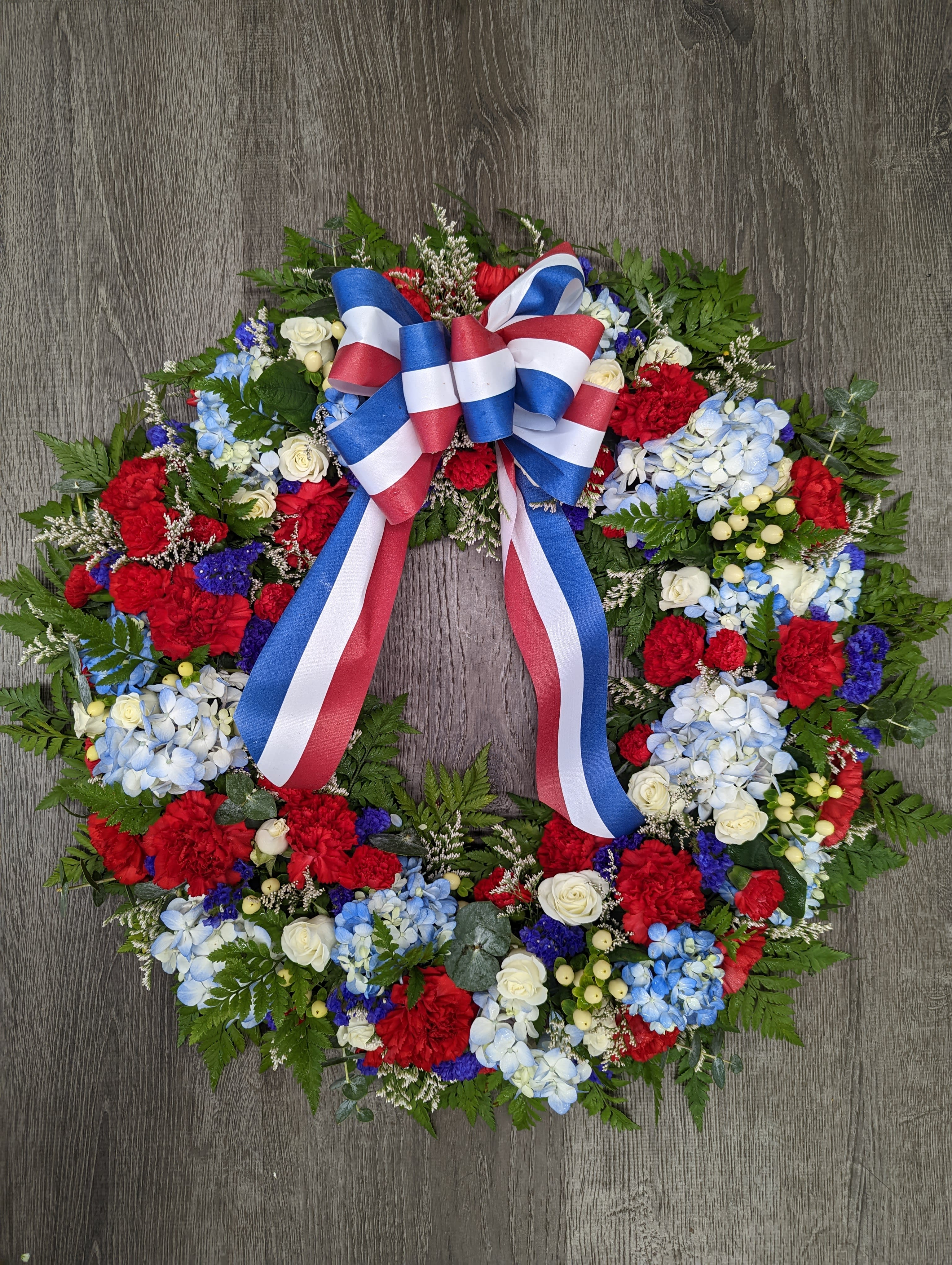 Circular floral wreath with red, white, and blue flowers and a ribbon bow