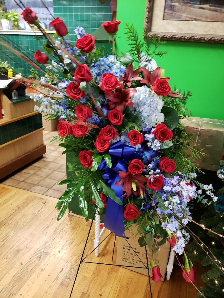 Large standing floral spray with red roses, blue hydrangeas, and lilies