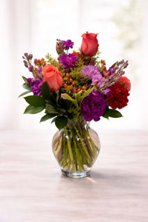 Mixed bouquet of coral roses and purple flowers in a clear glass vase