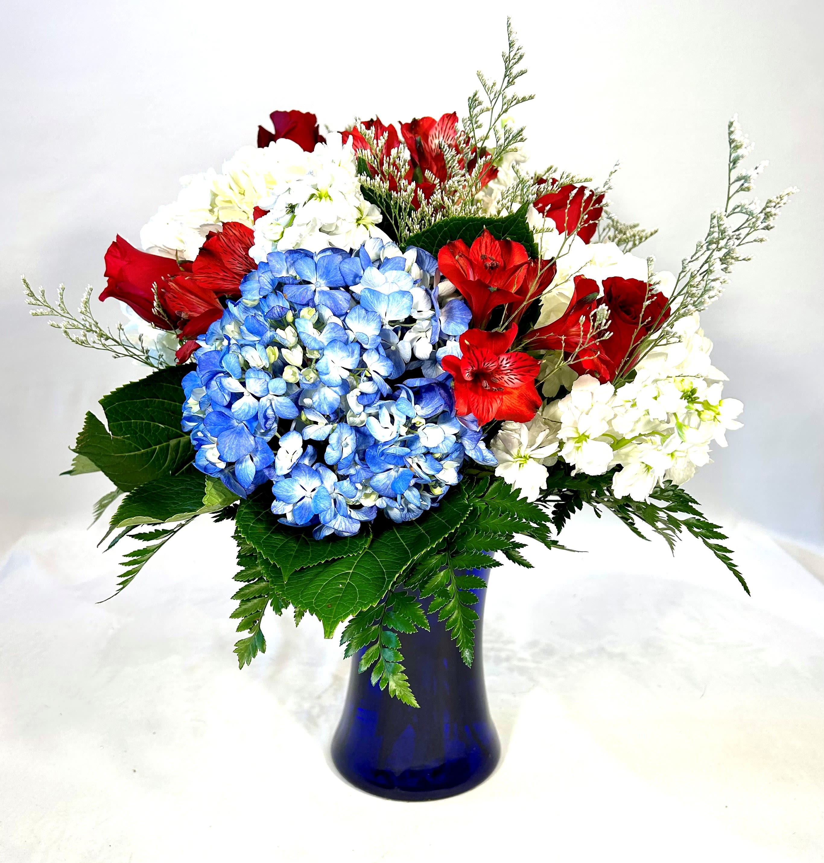 Bouquet of red roses, blue hydrangeas, and white flowers in a blue vase