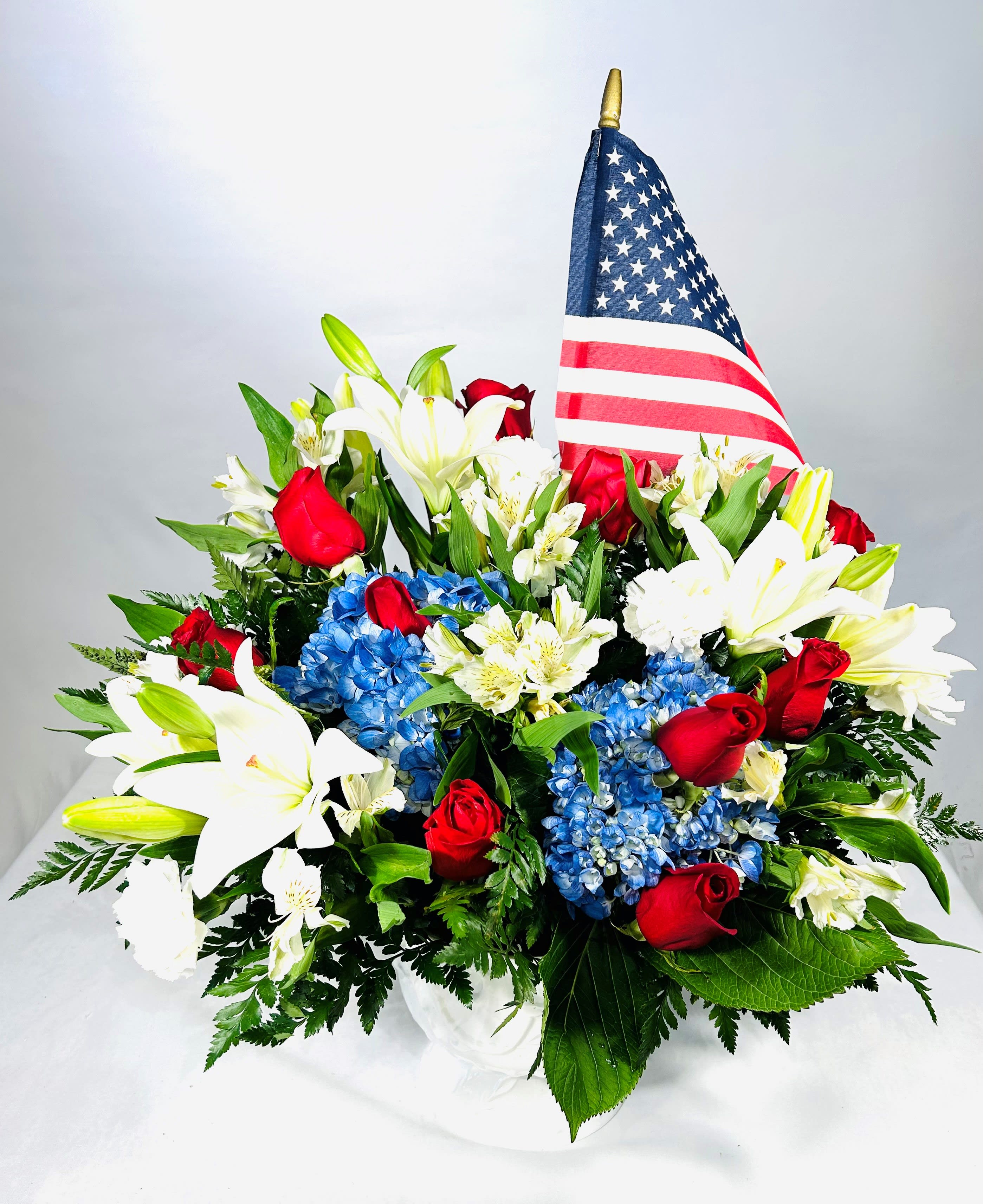 Salute to the Red, White &amp; Blue - This beautiful white basket of flowers is perfect for any patriotic occasion! The beautiful white, radiant red, and brilliant blue flowers are a stunning combination and will be sure to bring joy and happiness to whomever receives them. Comes with American Flag.  32" Tall