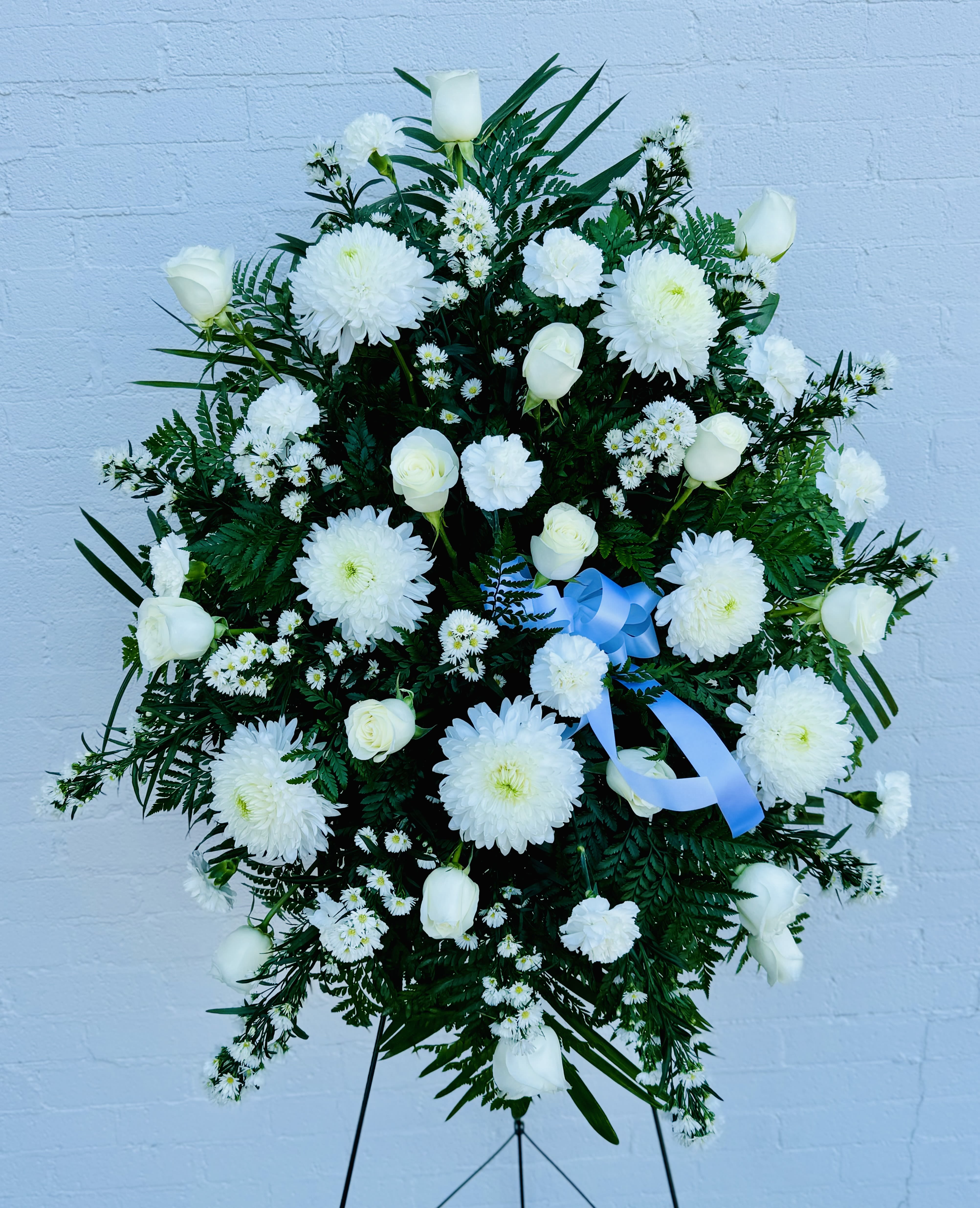 White floral standing spray with roses, chrysanthemums, and a blue ribbon