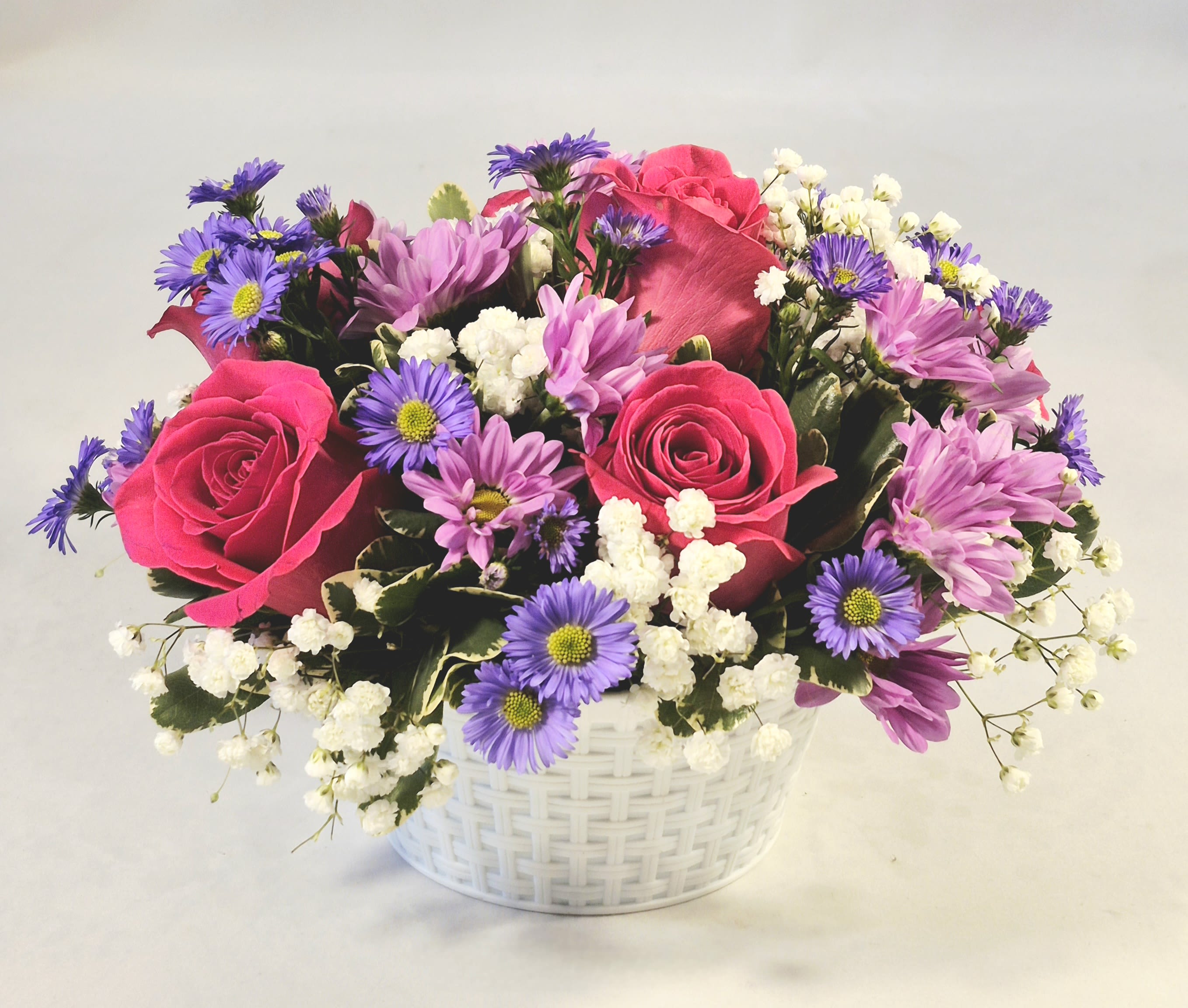 Pink roses and purple daisies in a white basket