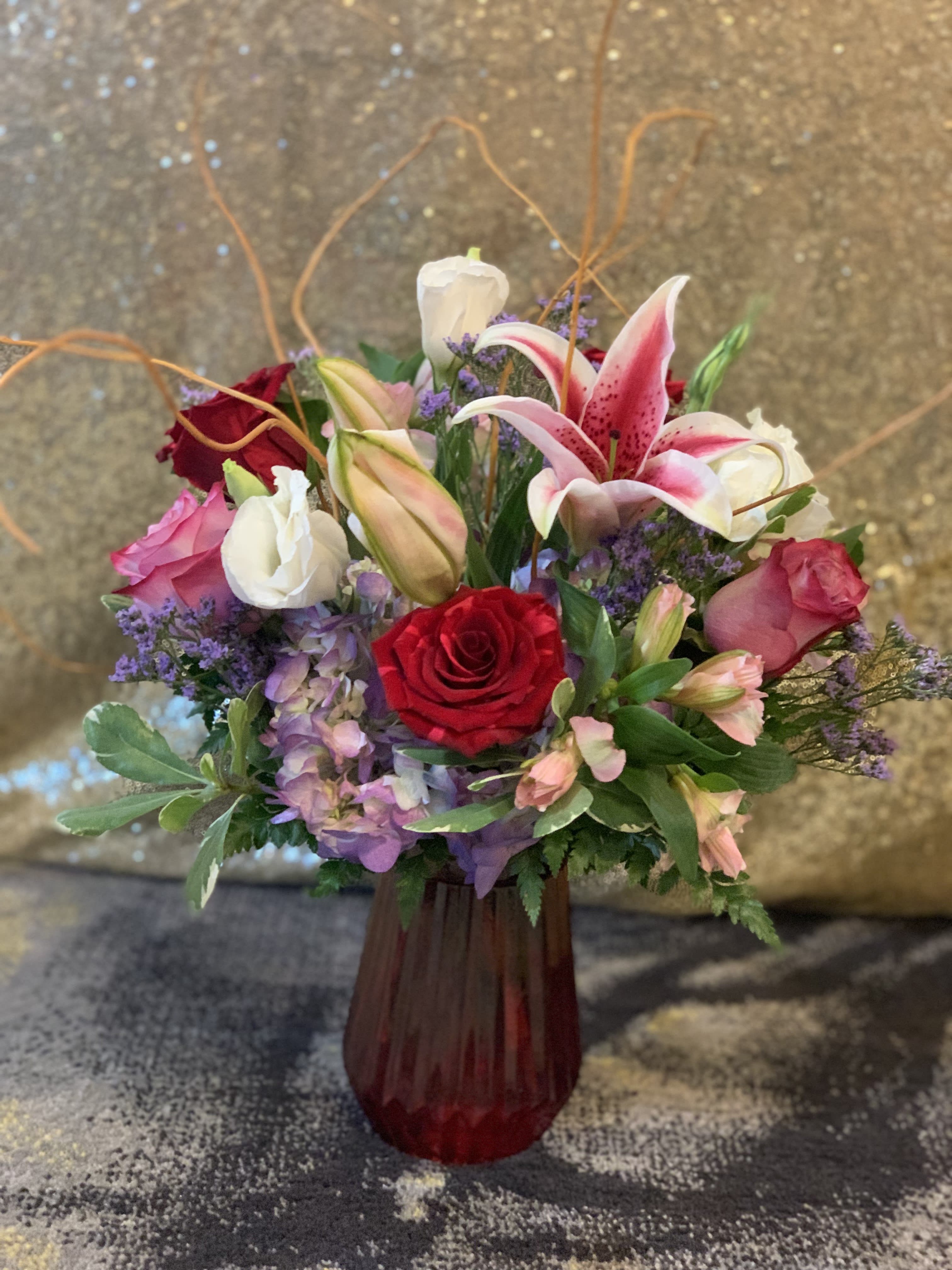 Mixed bouquet of roses, lilies, and purple flowers in a red vase