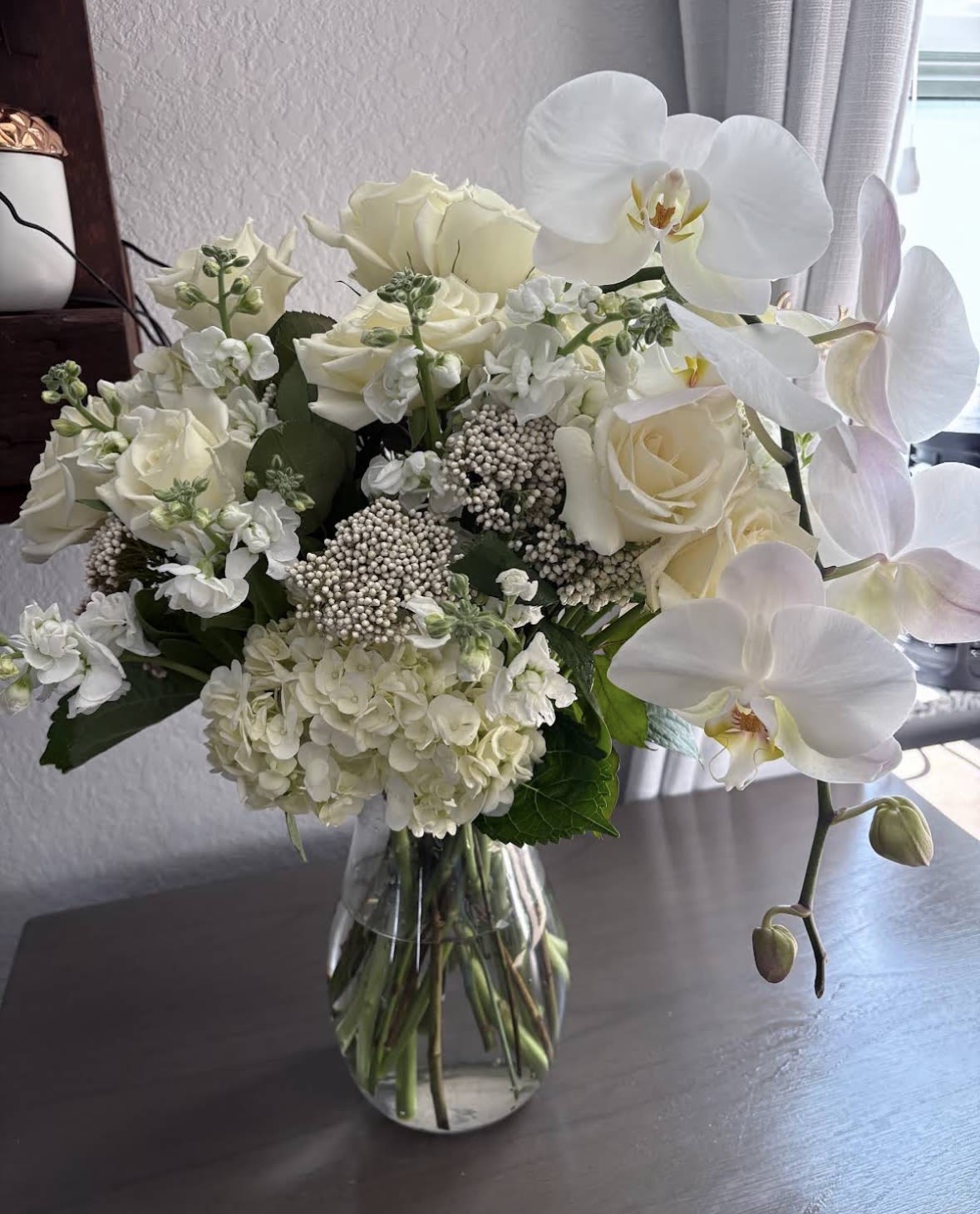 White roses, hydrangeas, and orchids arranged in a glass vase