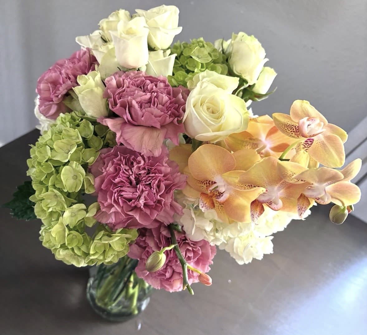 Bouquet of pink carnations, white roses, green hydrangeas, and orange orchids in a glass vase