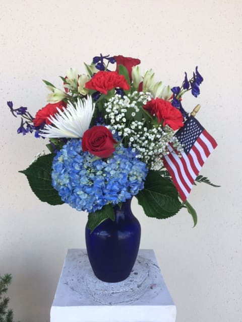 Red, white, and blue floral arrangement in a blue vase with an American flag
