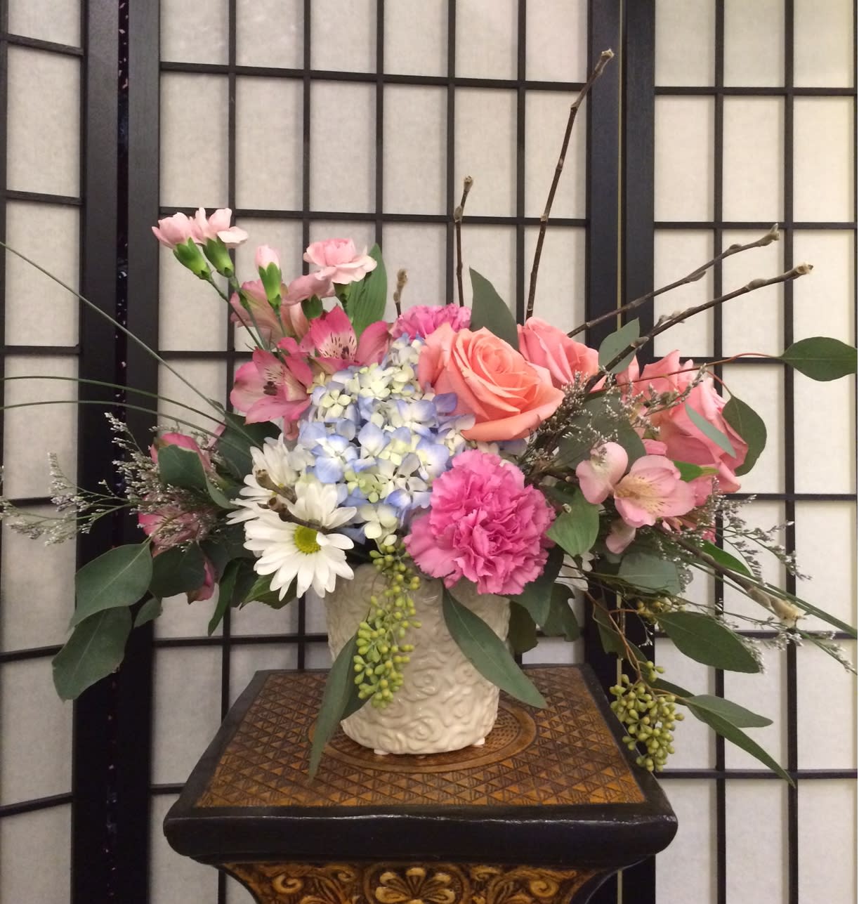 Pink and peach flowers arranged in a cream vase.
