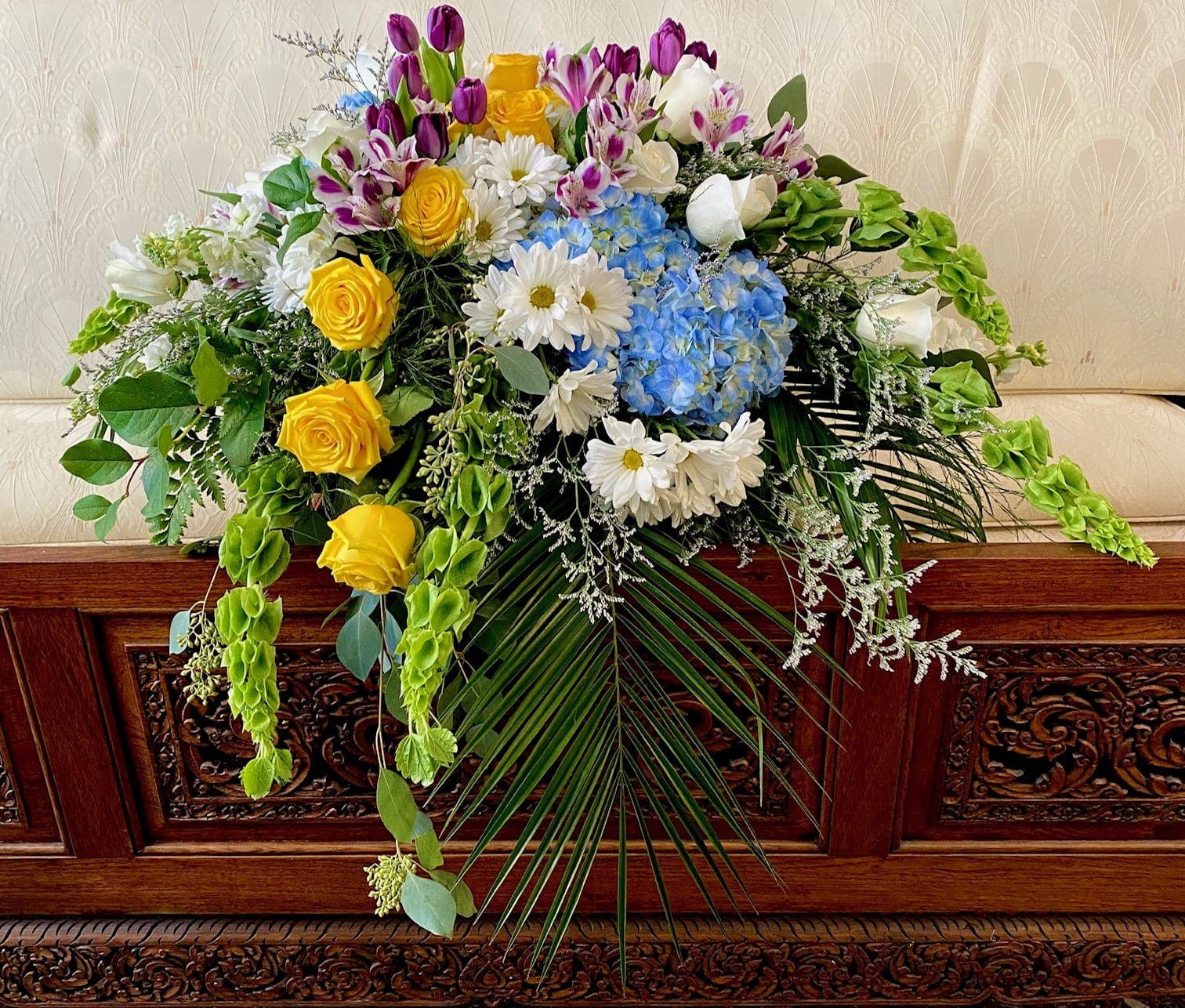 Large floral spray with yellow roses, blue hydrangeas, and white daisies