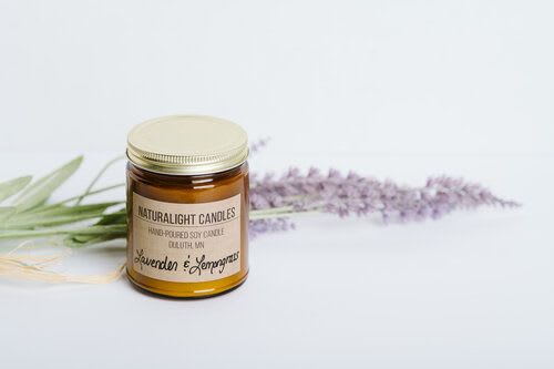 Amber jar soy candle with gold lid beside lavender sprigs on a light surface