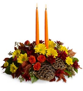 Harvest Glow - The charming centerpiece includes orange spray roses, burgundy cushion spray chrysanthemums, yellow daisy spray chrysanthemums accented with eucalyptus, lotus pods and salal. Includes two 12 orange taper candles. Approximately 16 1/2 W x 15 1/2 H