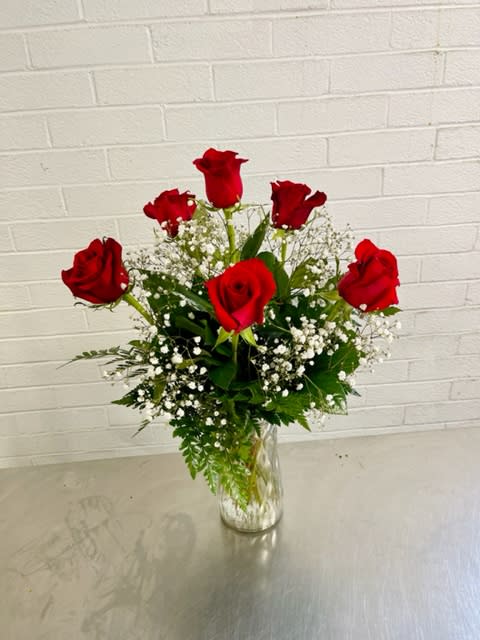 Red roses arranged in a clear glass vase with white filler flowers