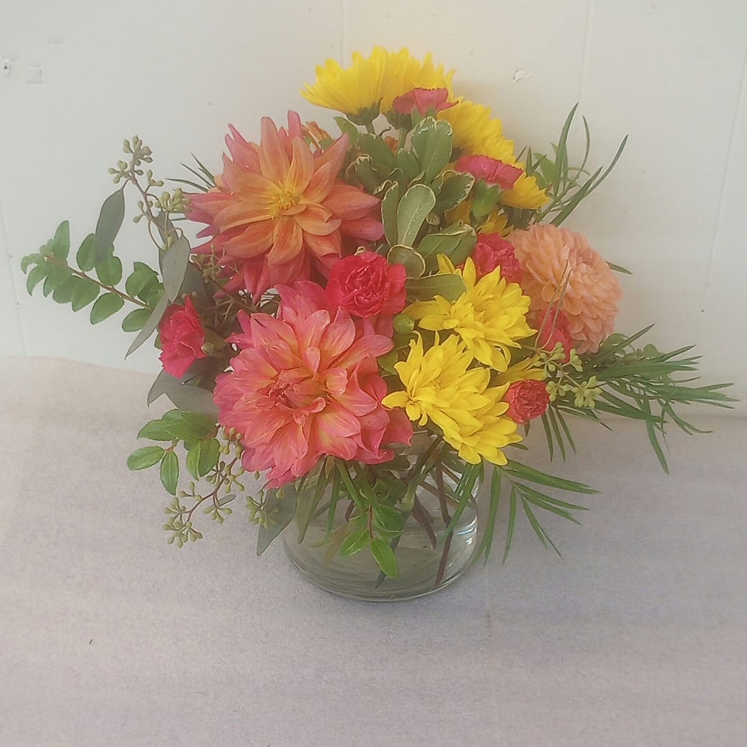 Mixed bouquet of pink, yellow, and peach flowers in a clear glass vase