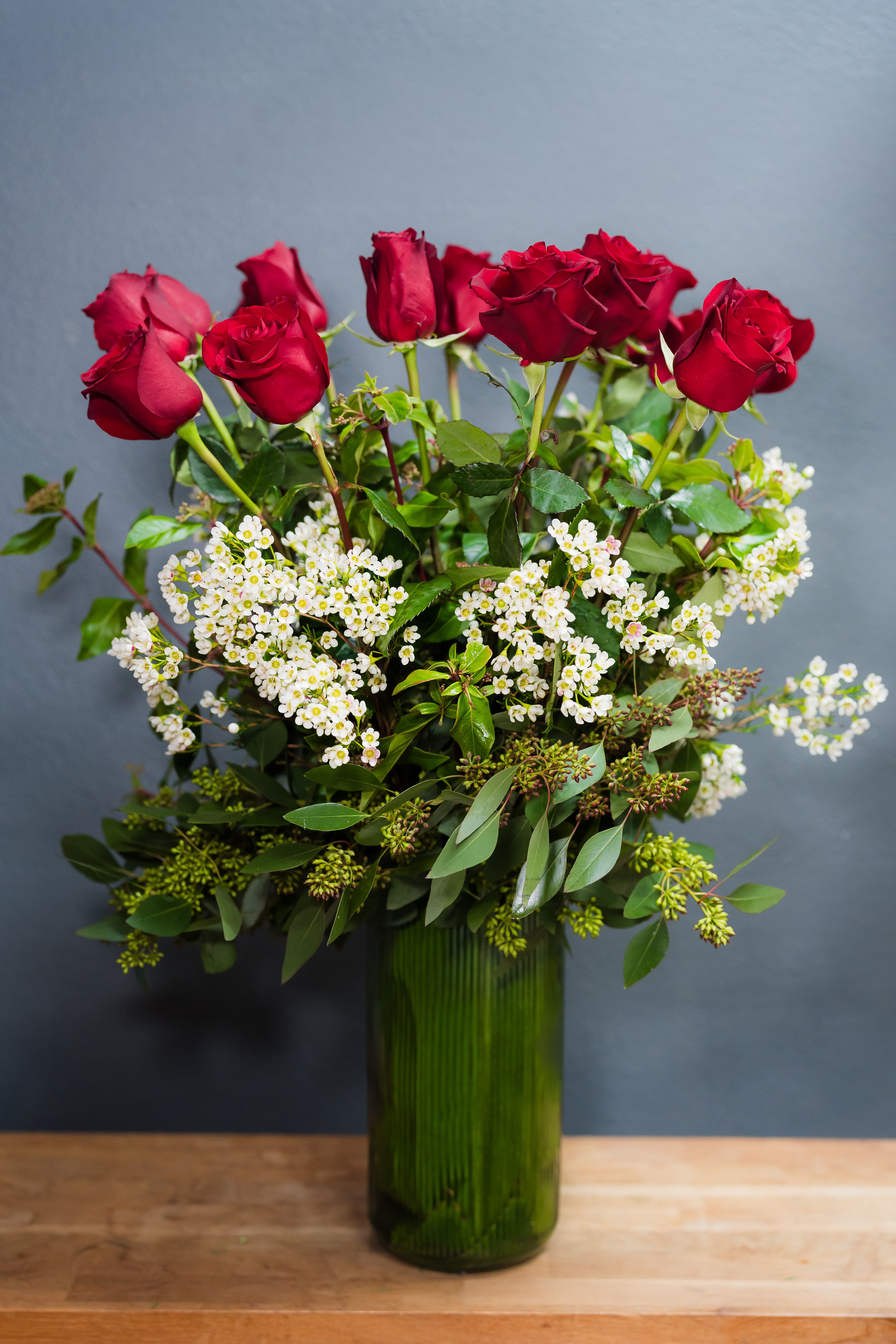 Red roses arranged in a green glass vase with white filler flowers