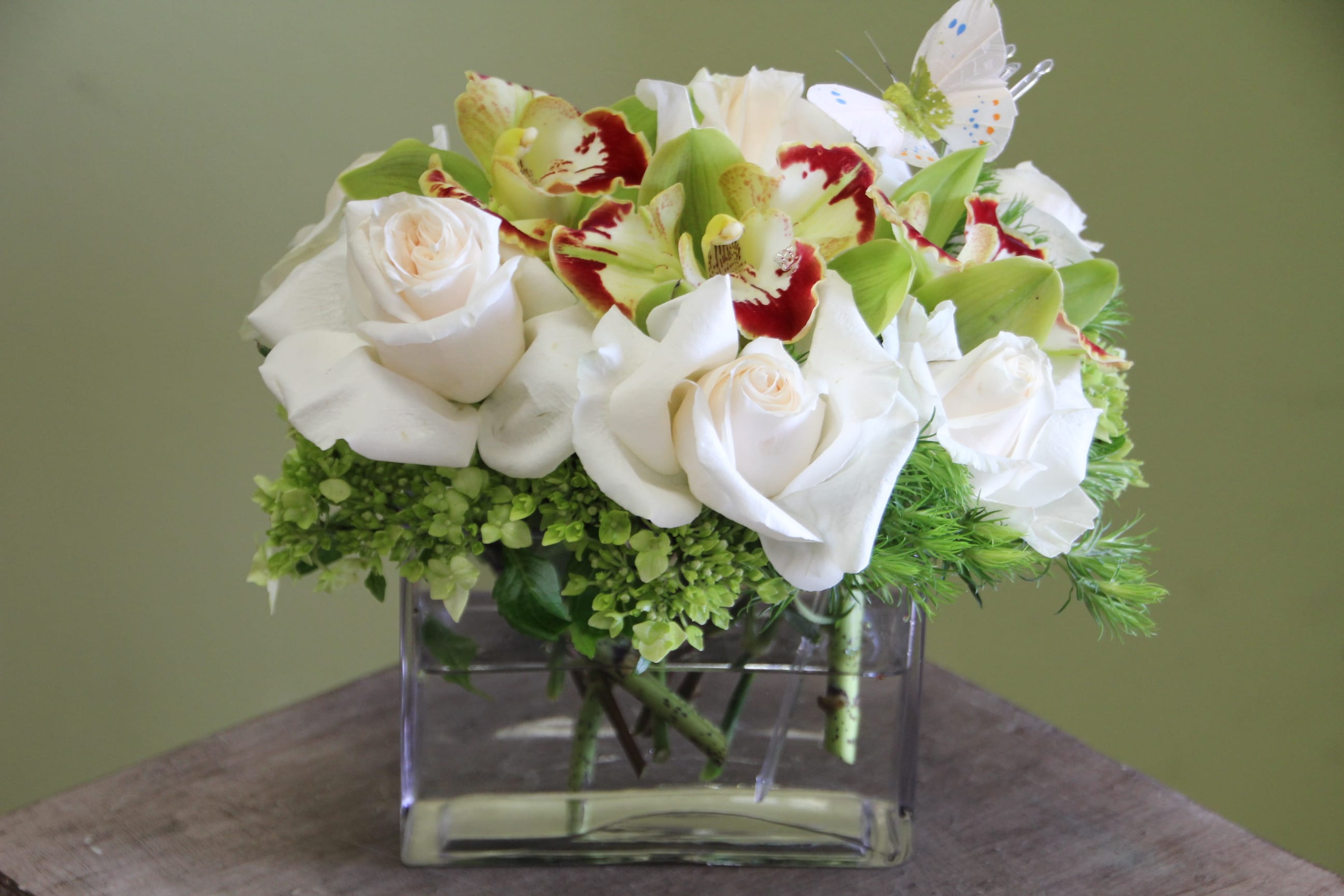 White roses and green orchids in a clear square vase