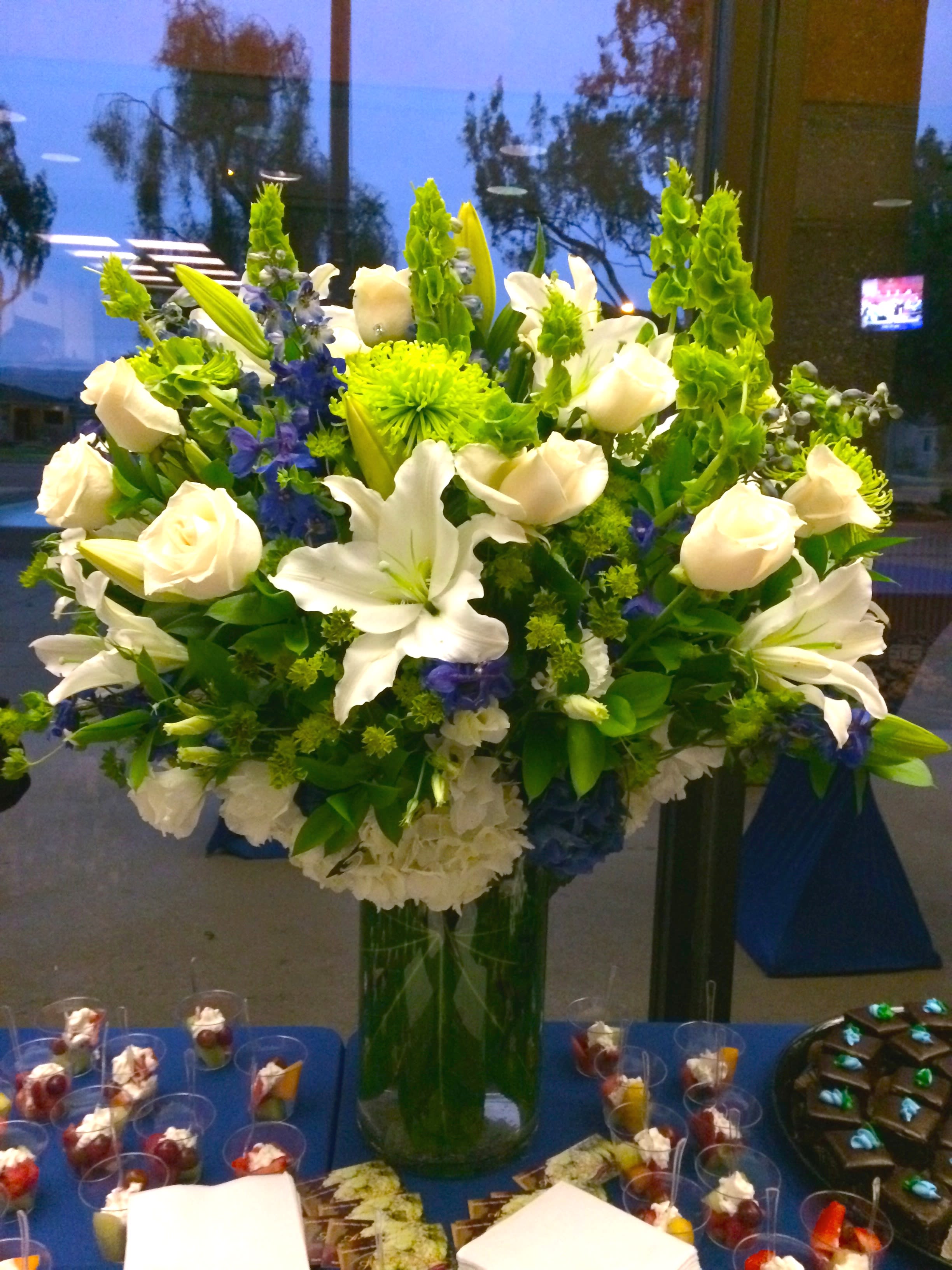 Large vase arrangement of white lilies and roses with green and blue flowers