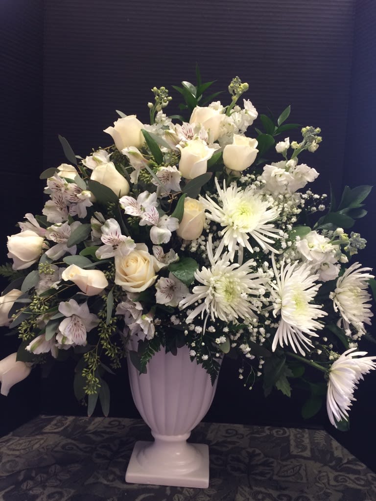 White roses and chrysanthemums arranged in a pale pedestal vase