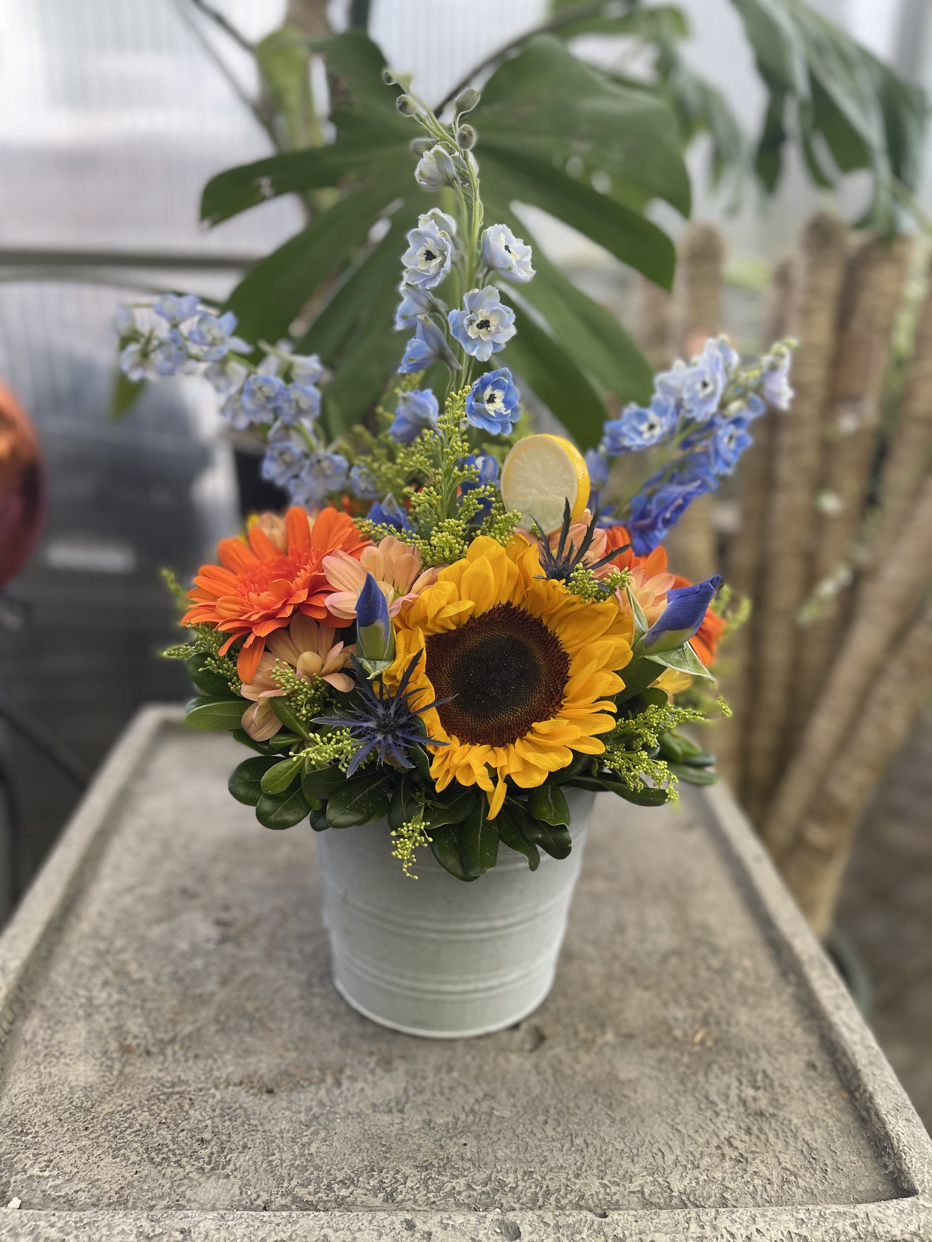 Bright mixed bouquet in a white metal bucket with a sunflower and blue flowers