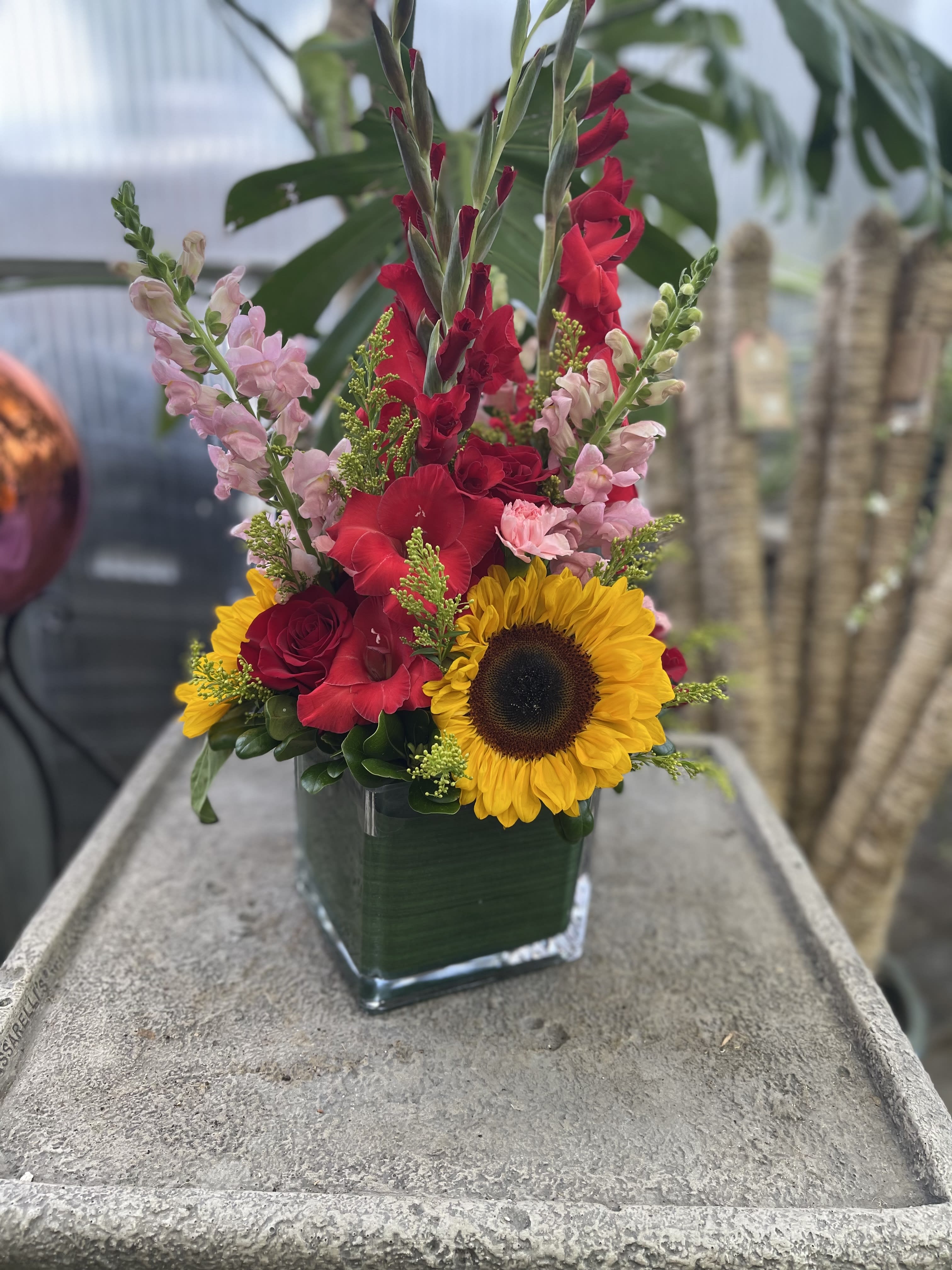 Tall mixed bouquet with sunflowers, red gladiolus, and pink snapdragons in a glass vase