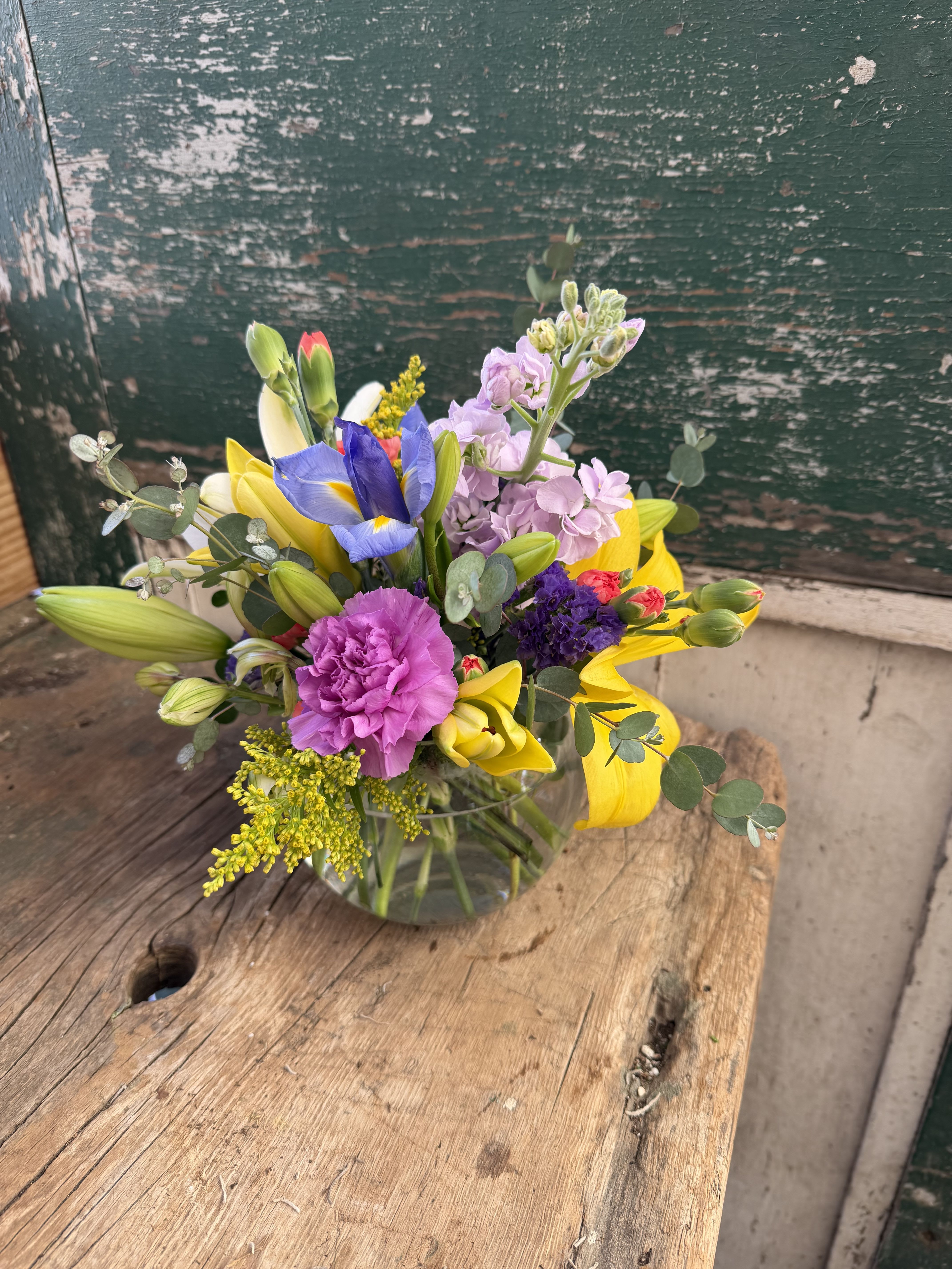 Mixed bouquet with yellow lilies, purple iris, and pink carnations in a glass vase