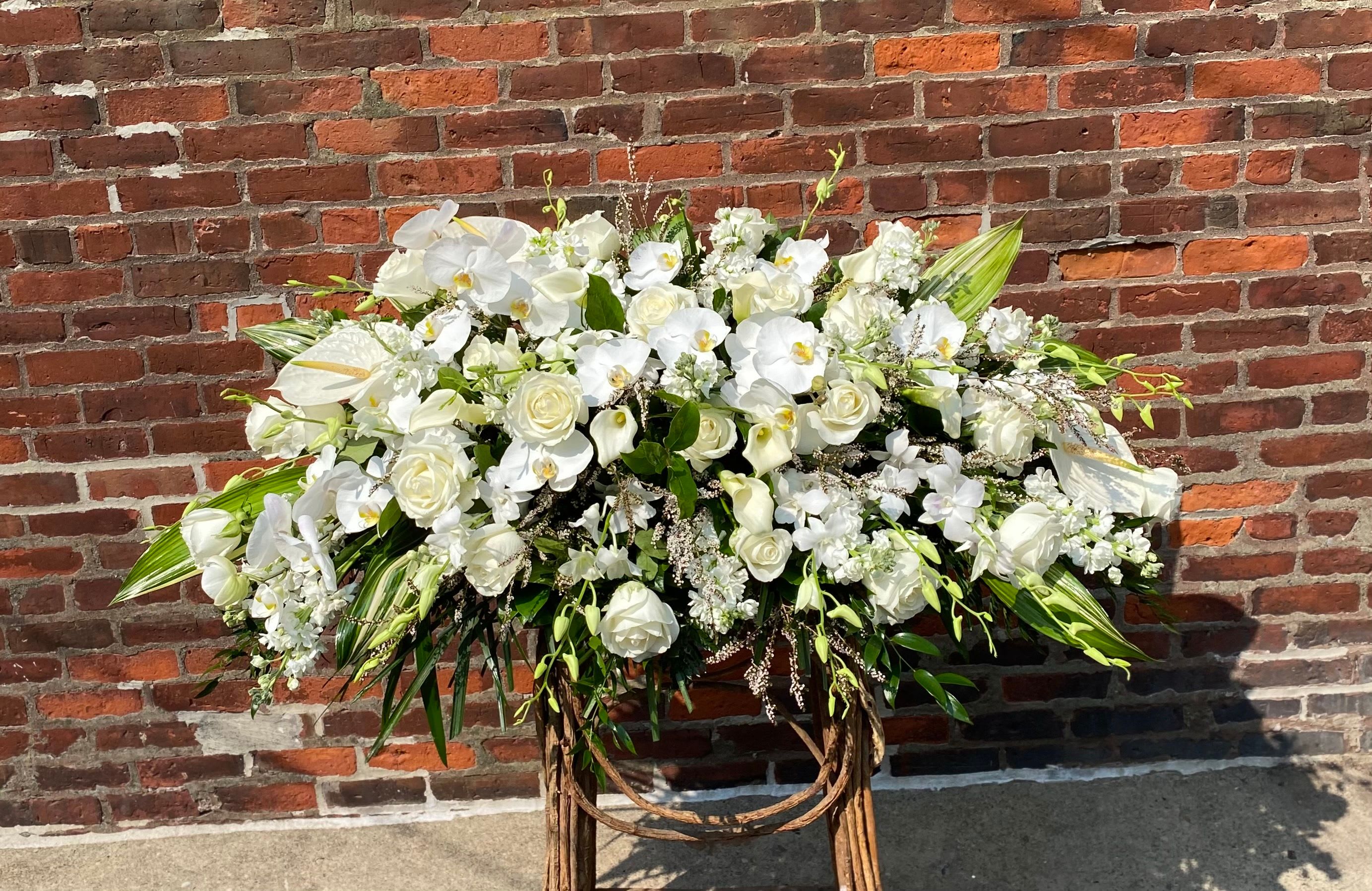 Large white floral arrangement on a stand against a brick wall