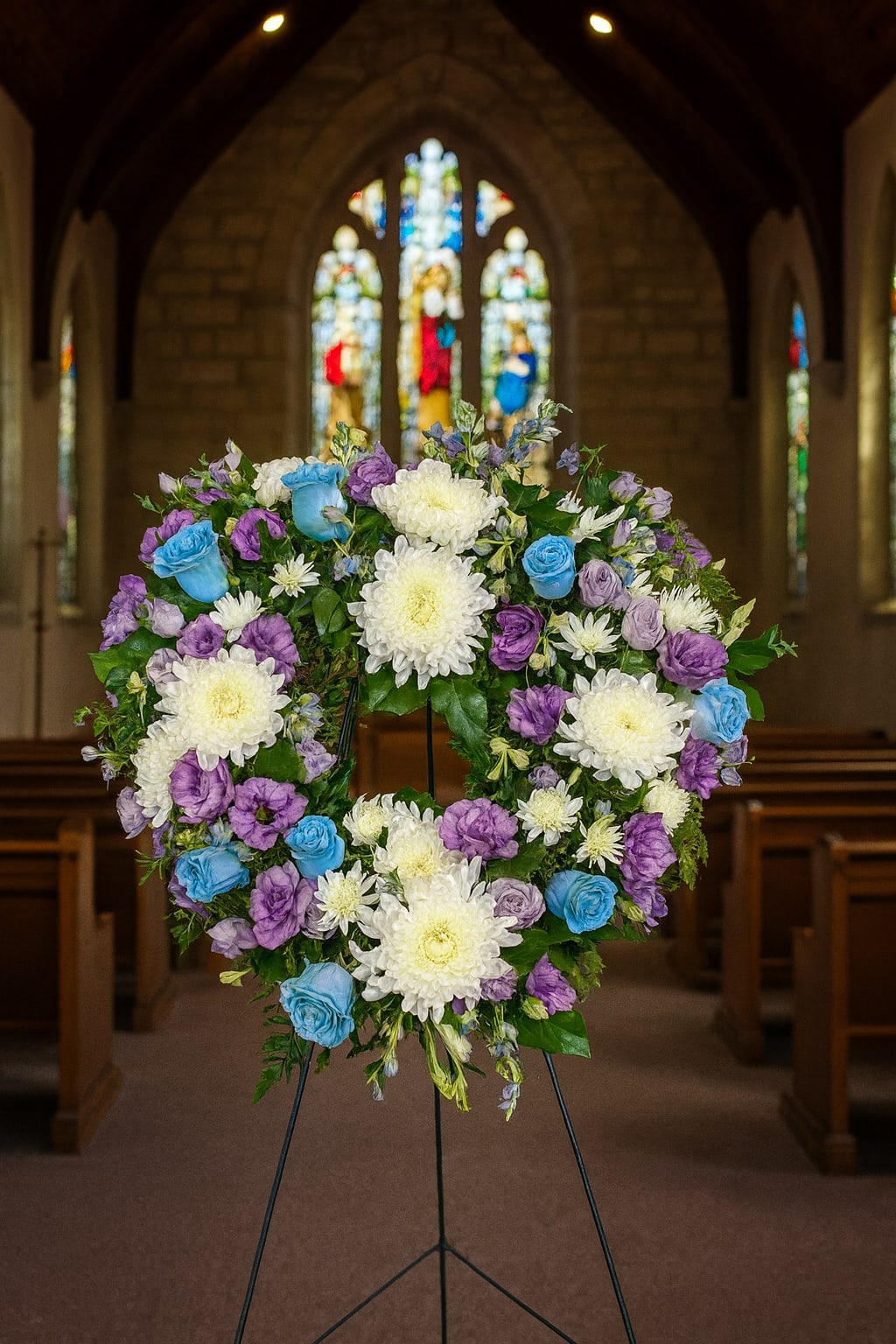 Heart-shaped floral wreath on a stand with white, purple, and blue flowers