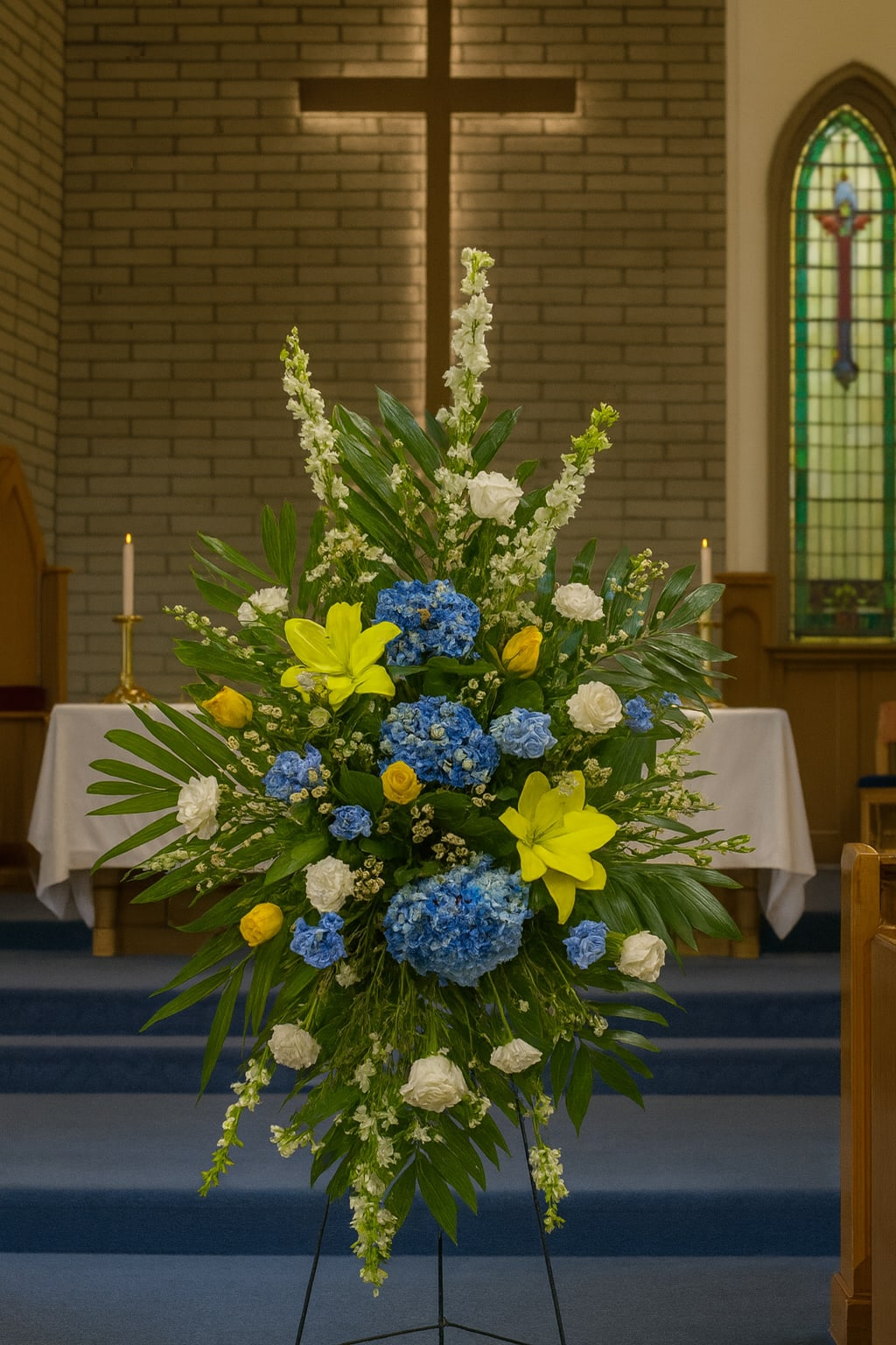 Tall floral spray with blue, yellow, and white flowers in a church