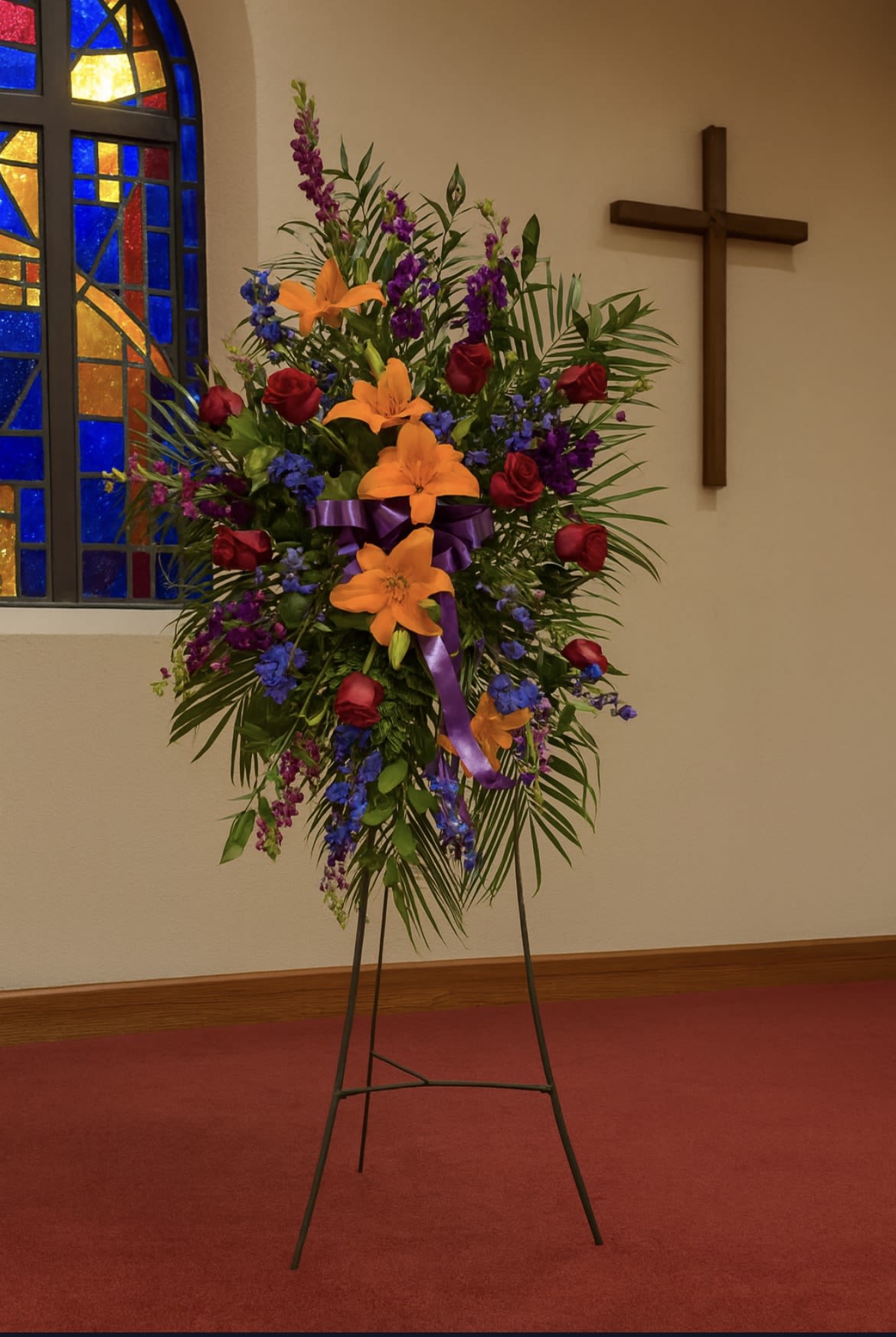 Standing floral spray with lilies, roses, and purple flowers on an easel