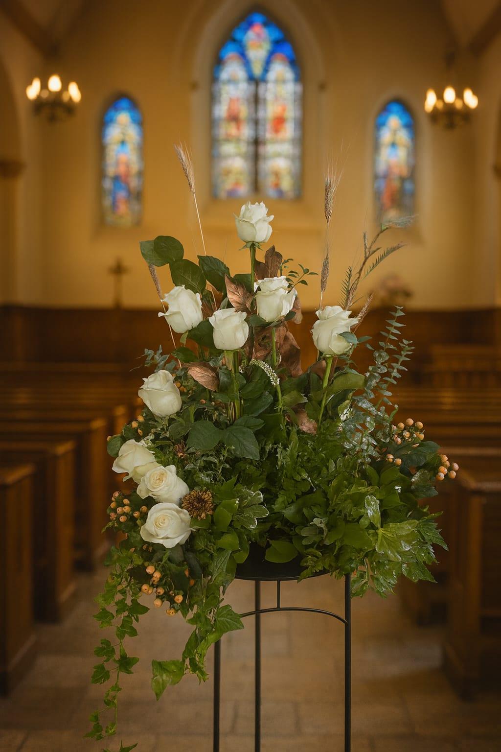 White roses arranged with greenery in a church setting