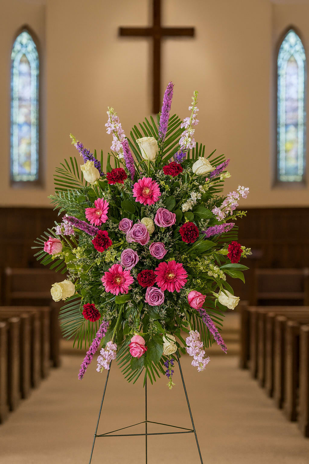 Tall floral spray with pink, purple, and white flowers on an easel in a church
