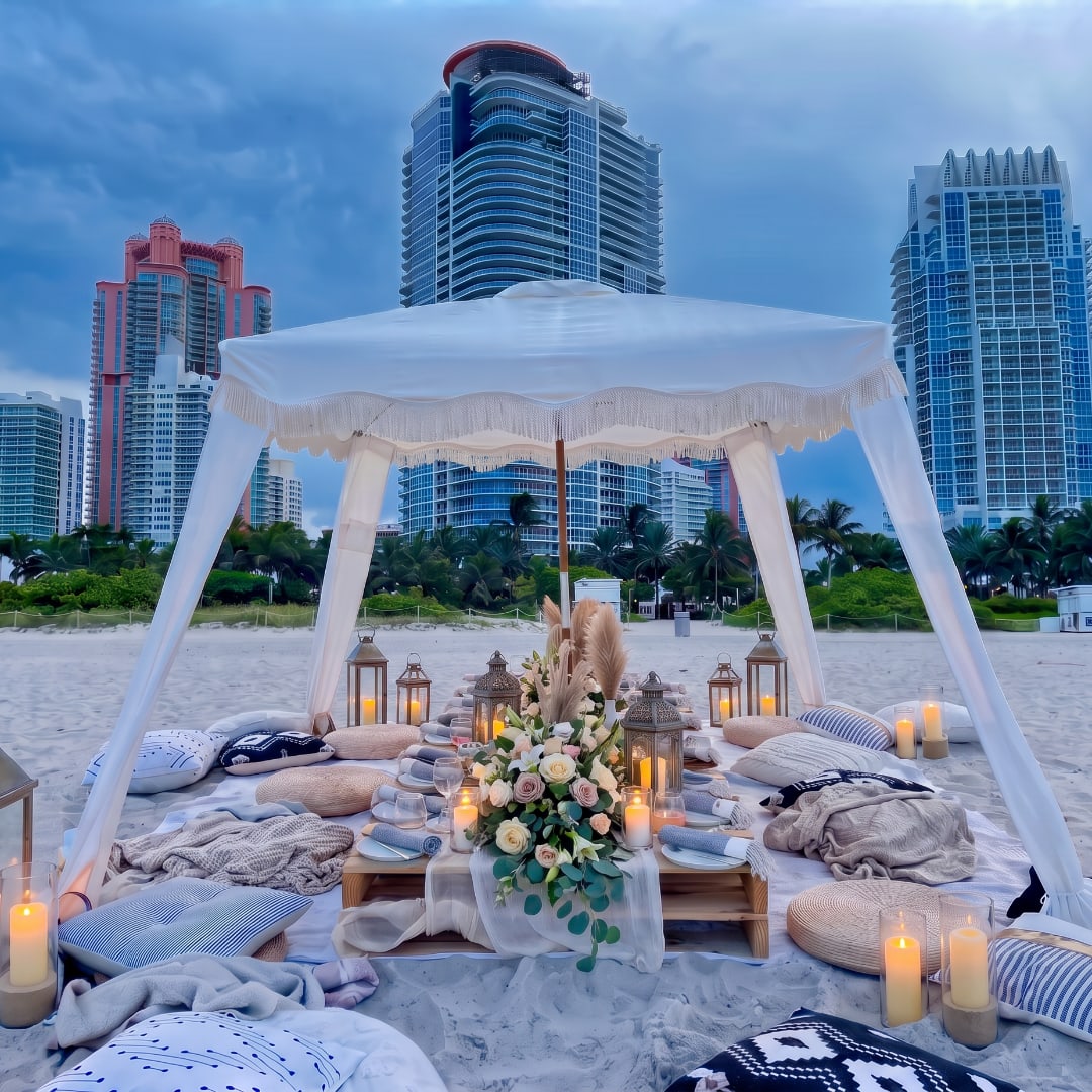Beach picnic setup with a floral centerpiece under a white canopy