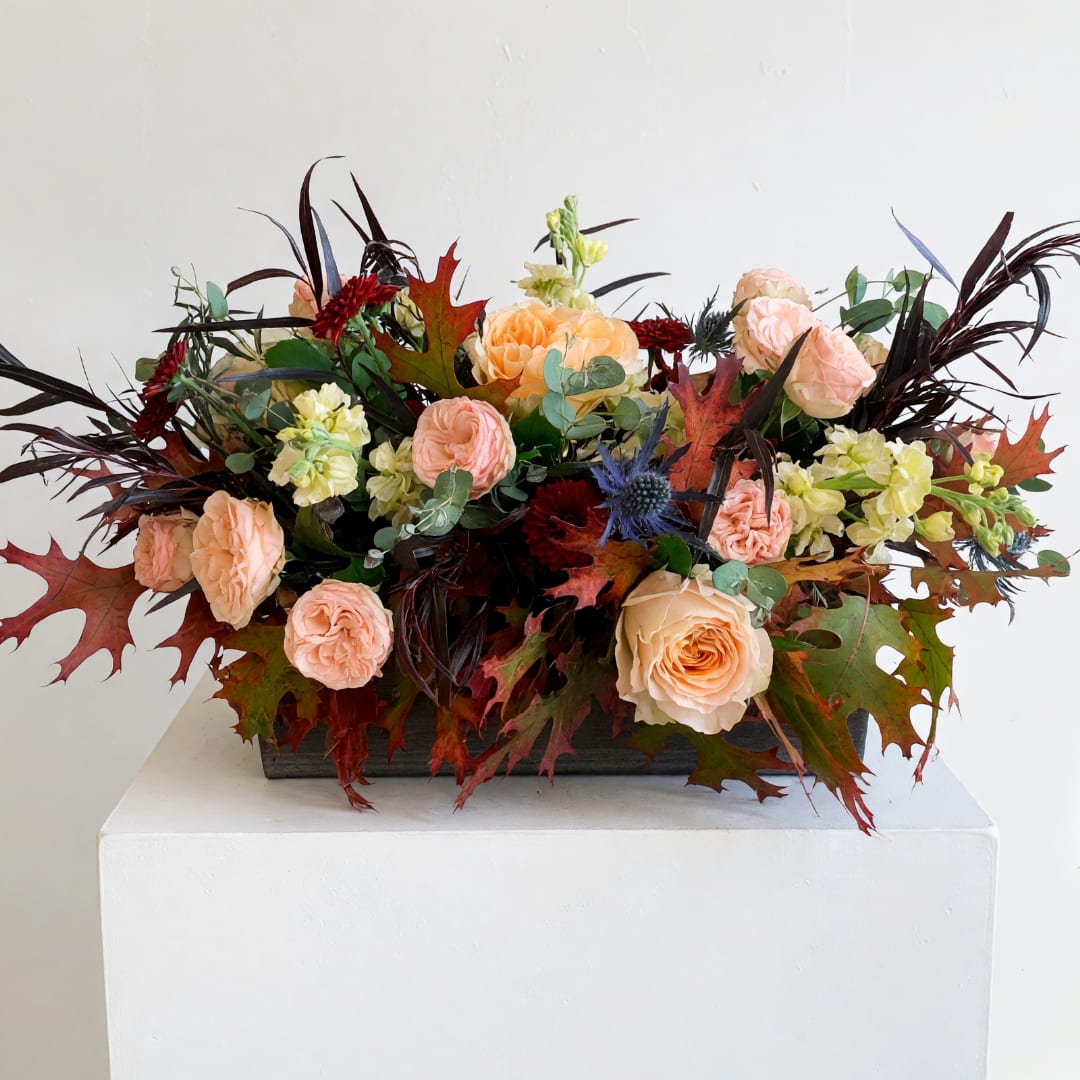 Peach roses and pale yellow flowers in a low rectangular arrangement