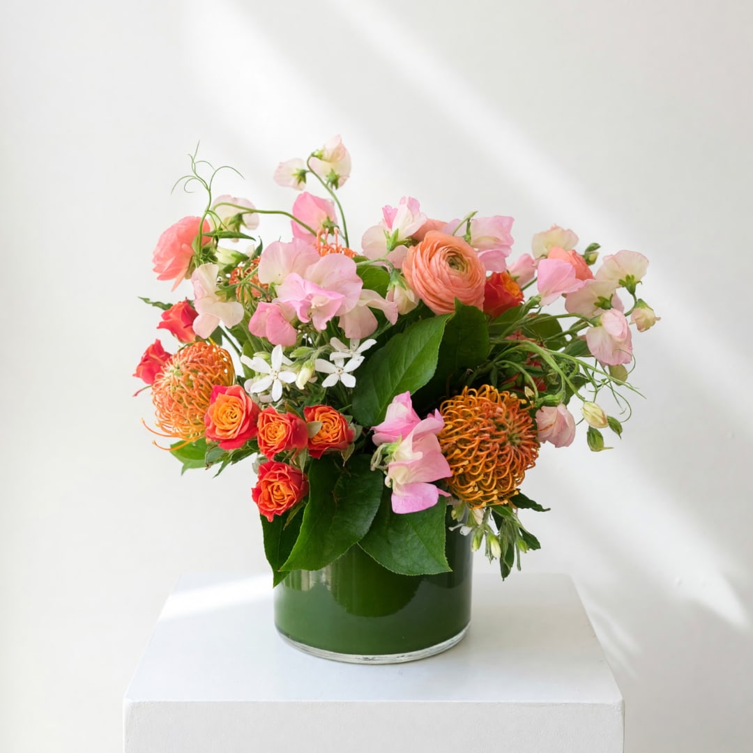 Mixed pink and orange flowers arranged in a green glass vase