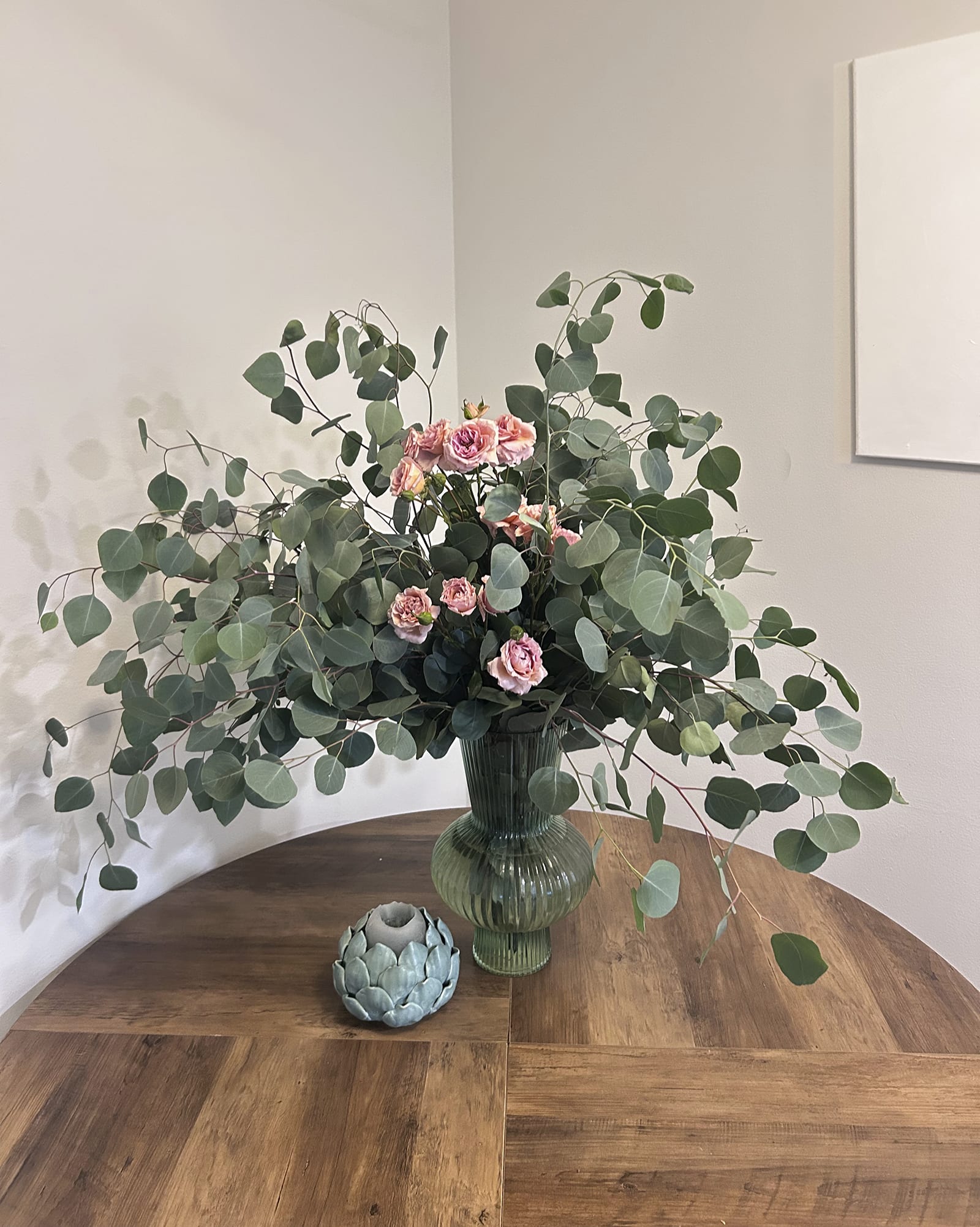 Pink spray roses in a green glass vase with large eucalyptus branches