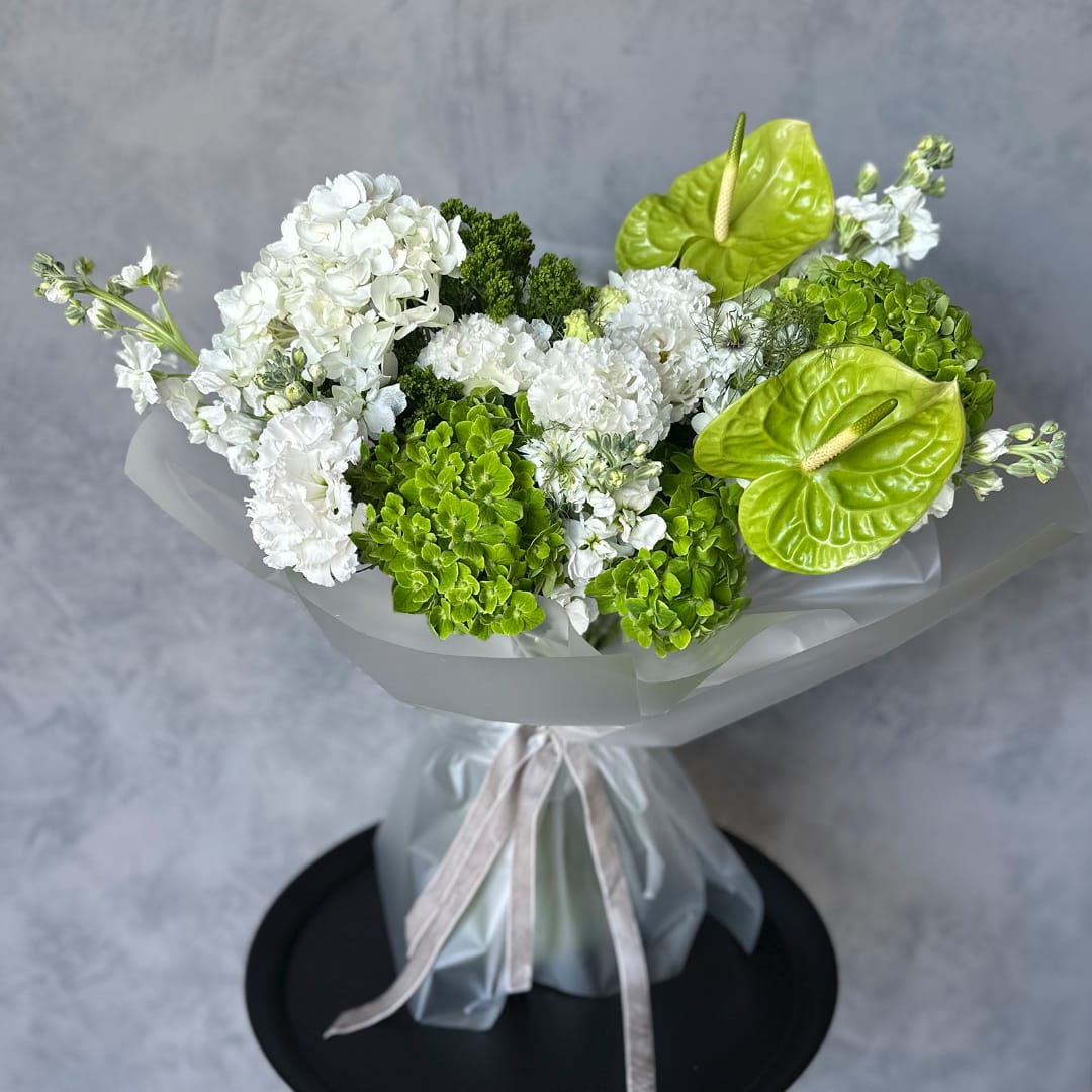 White and green bouquet with hydrangeas and anthuriums wrapped in sheer paper