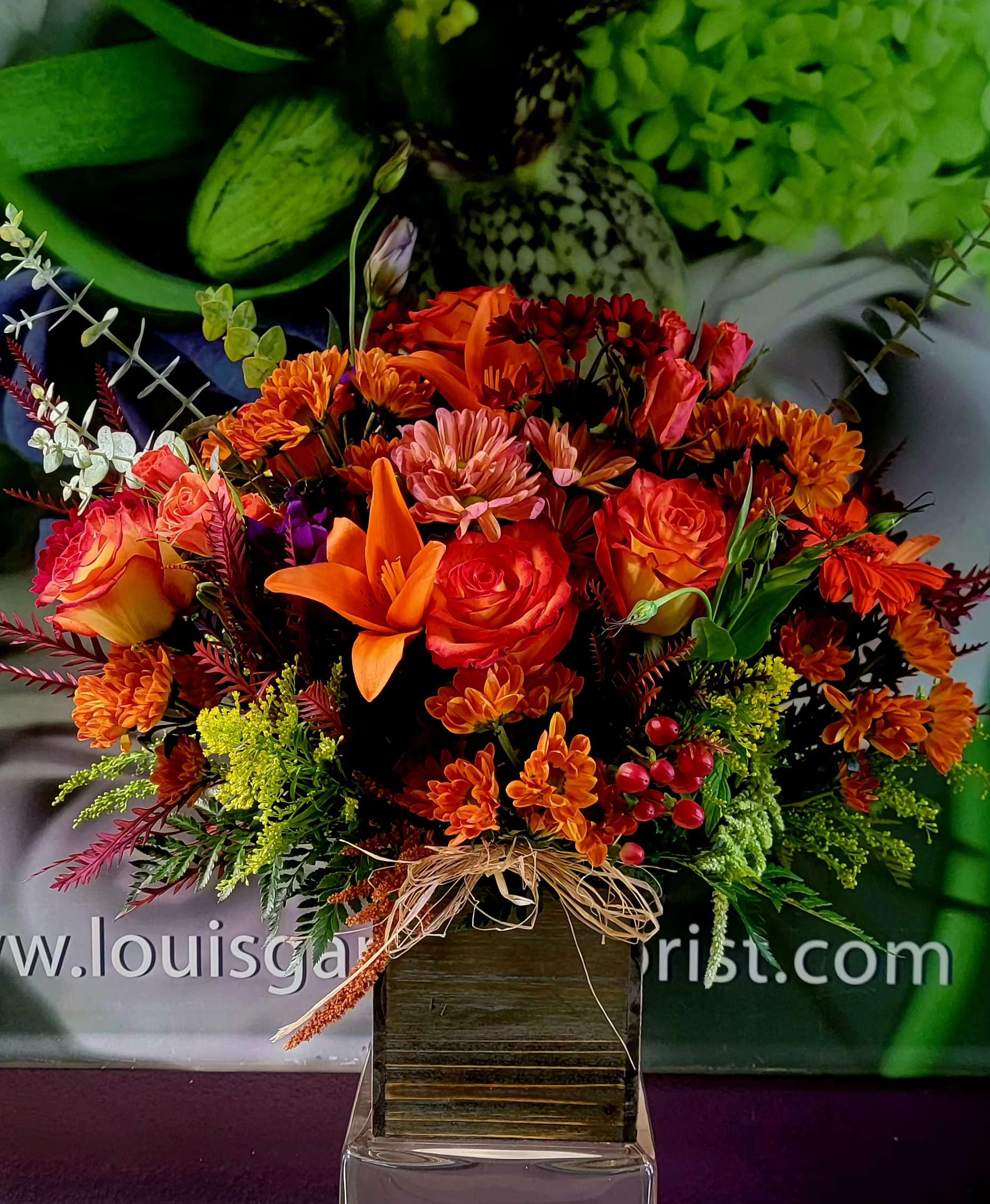 Orange and red mixed flower arrangement in a square vase