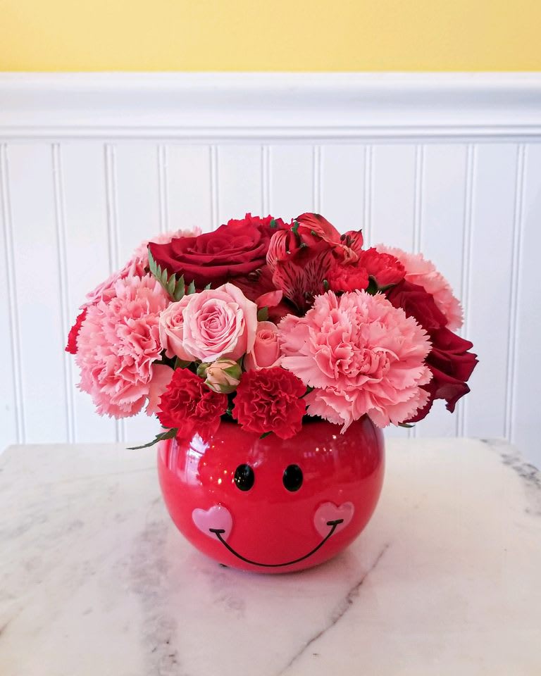 Pink and red flower arrangement in a smiley-face vase