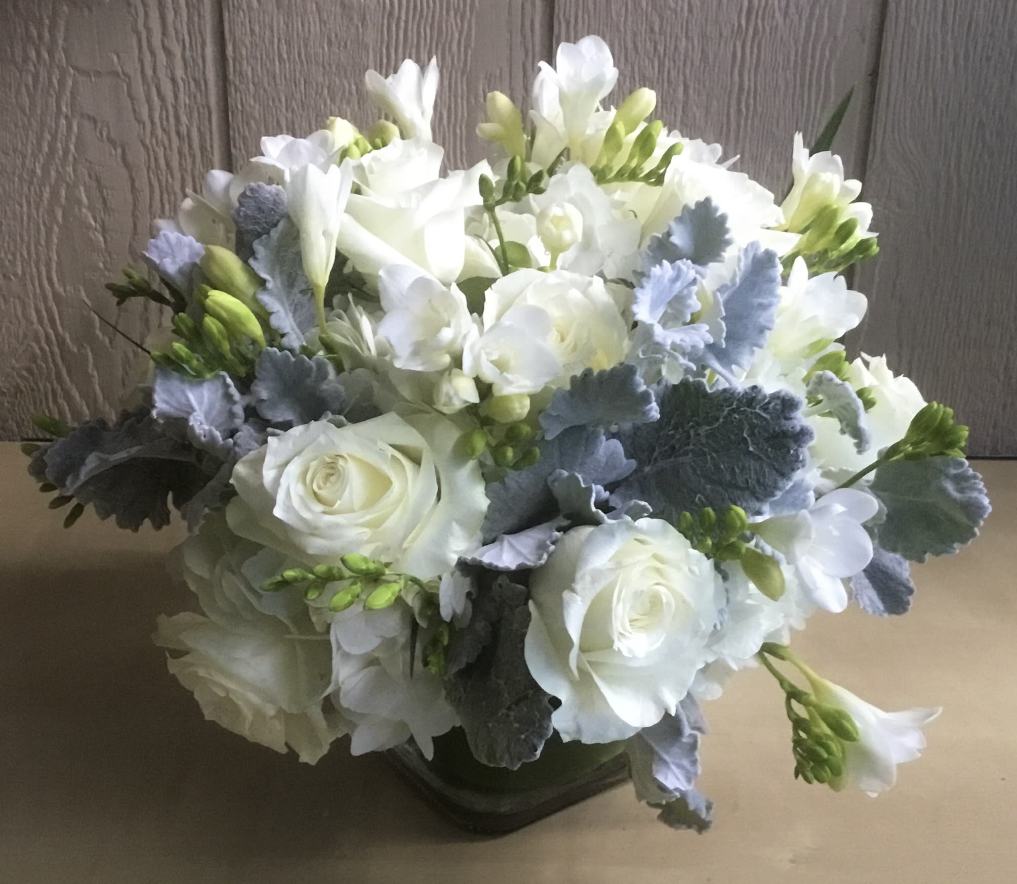 White roses and freesia arranged with blue-gray foliage in a low vase