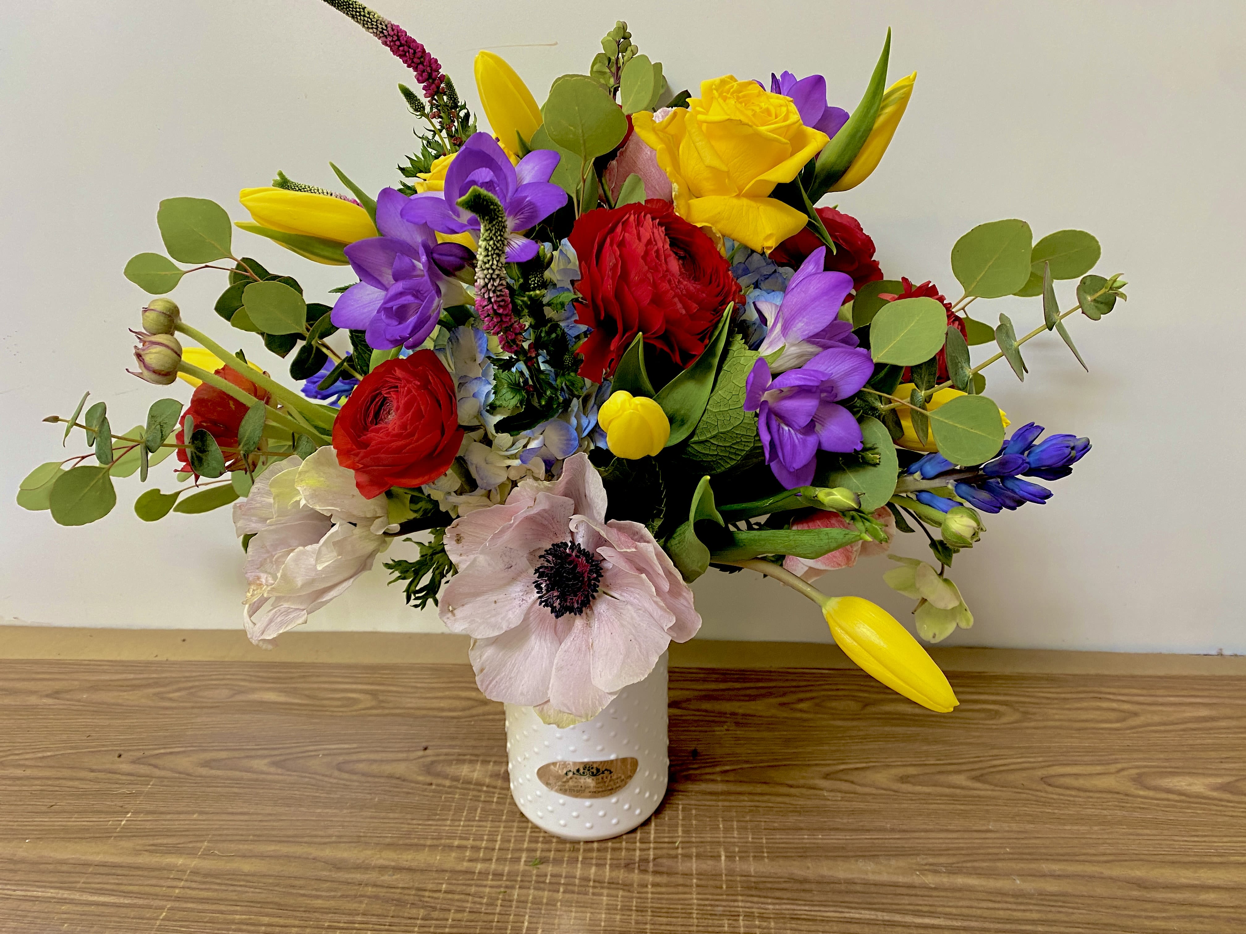 Colorful mixed bouquet in a white vase with red, yellow, purple, and pale pink blooms