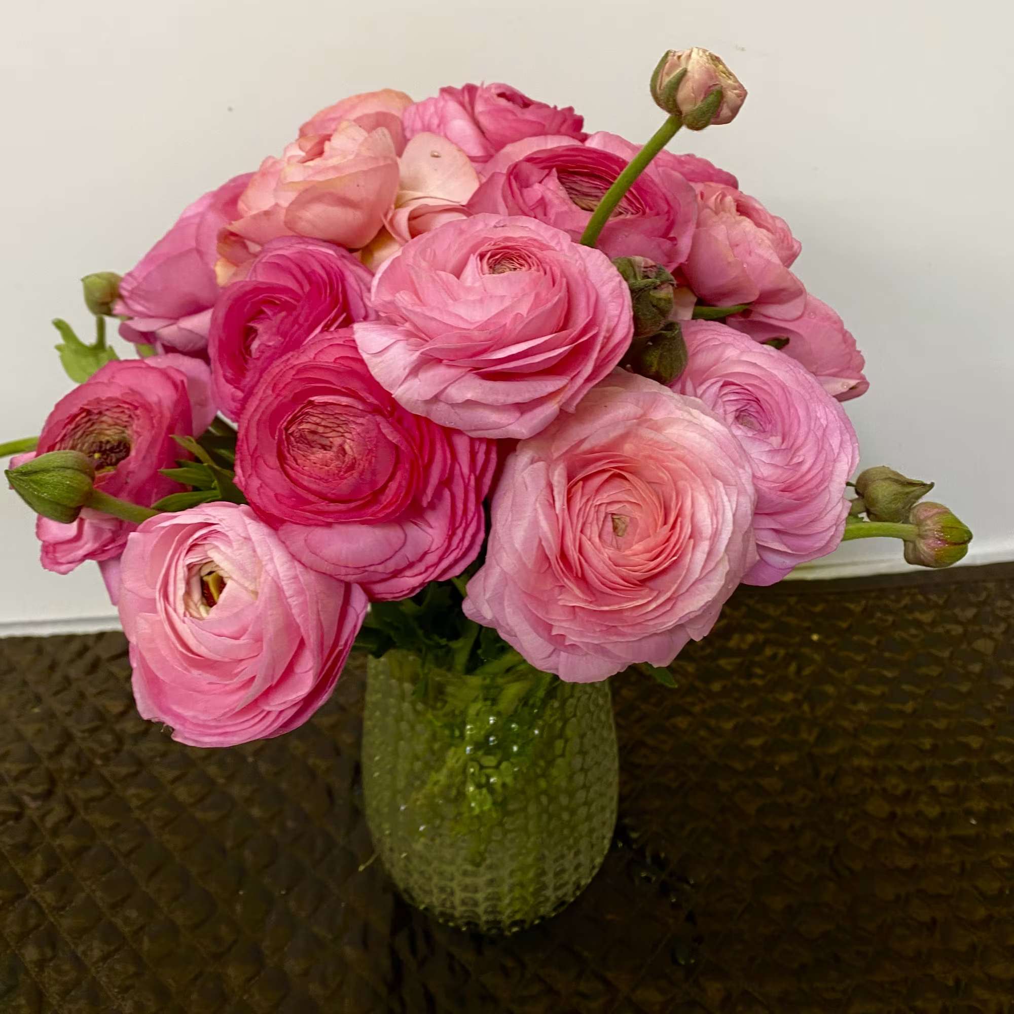 Pink ranunculus bouquet in a green glass vase