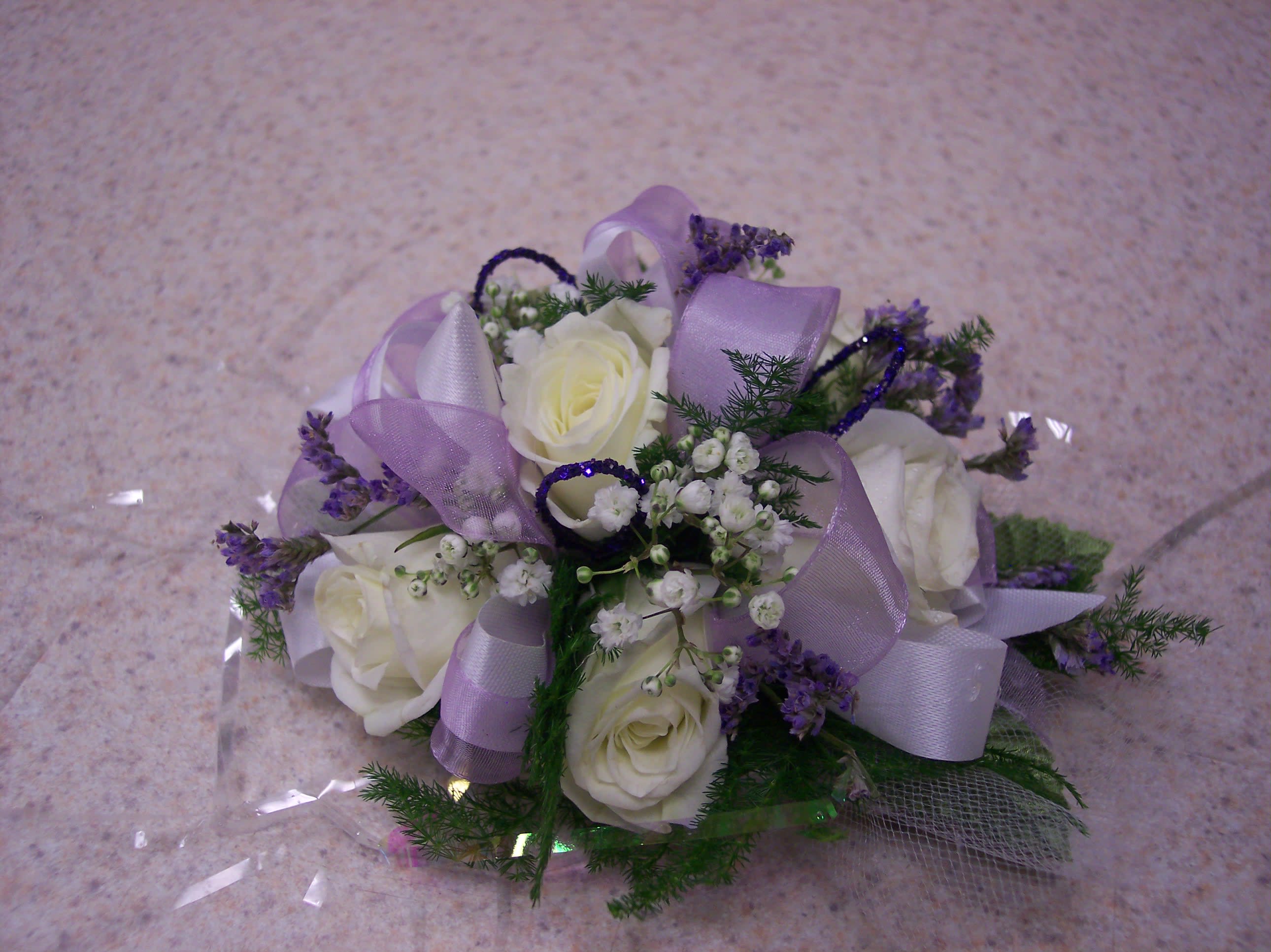 Corsage - Wrist - MAKE NOTES OF COLORS IN THE SPECIAL INSTRUCTION SECTION.  Make that lasting impression at this years Homecoming or Prom with our lovely 7-rose placement wristlet corsage adorned with colorful gems or glitter strands. Don’t settle for skimpy 3 or 5 rose placements offered by other florists. Our stunning and sophisticated white rose corsage goes beautifully with any dress color. Flowers, ribbons, gems and glitter strands are available in many colors. Orders are for pick-up only.