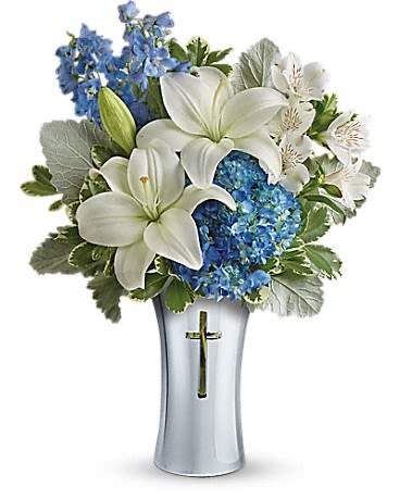 White lilies and blue flowers arranged in a silver vase with a cross