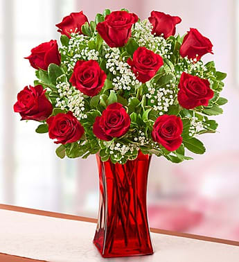 Red roses arranged in a red glass vase with white filler flowers