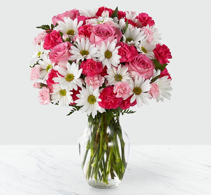 Pink roses, white daisies, and pink carnations arranged in a clear glass vase