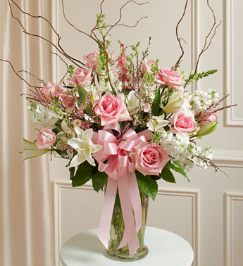 Pink roses and white lilies in a clear glass vase with a pink ribbon