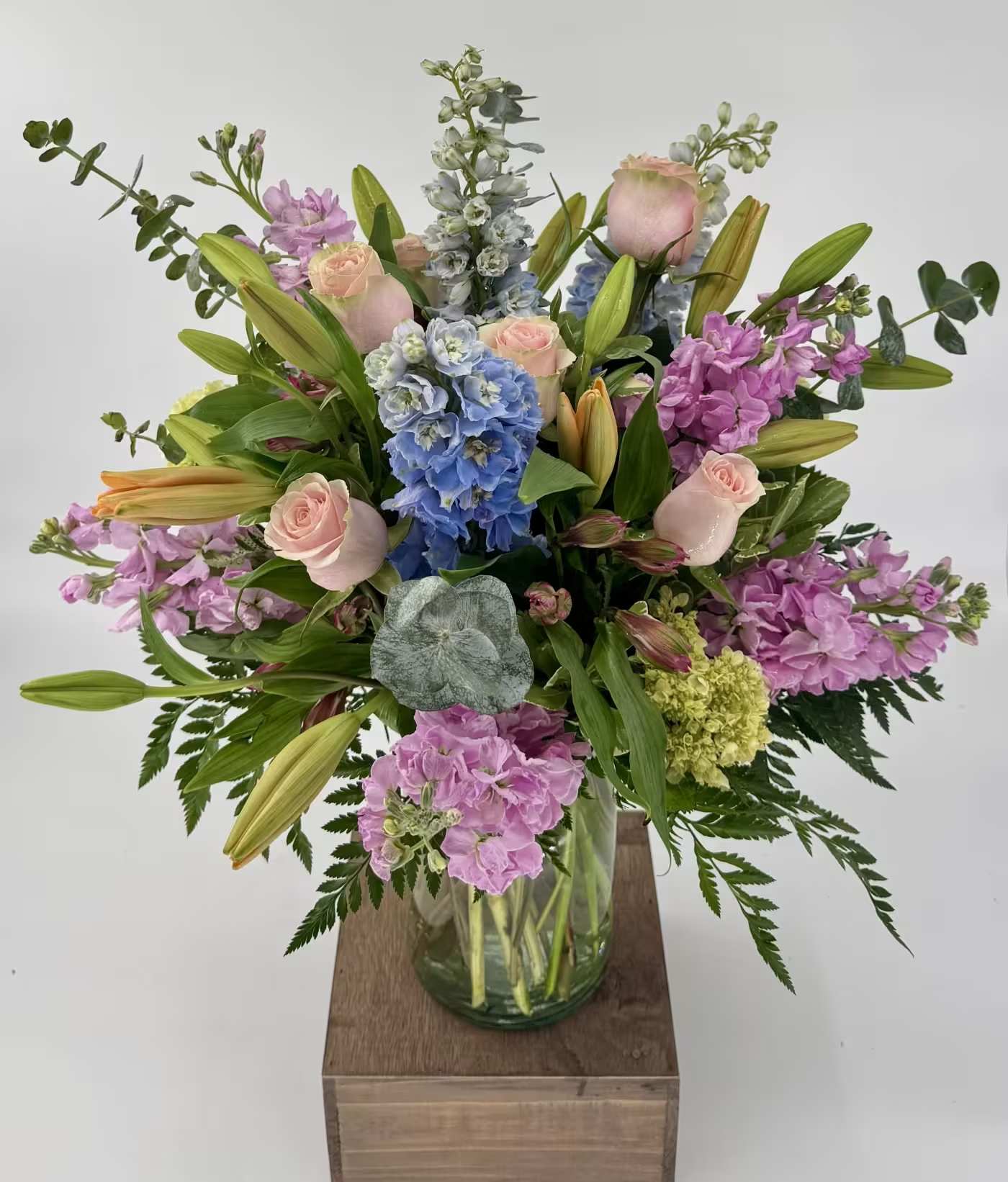 Mixed bouquet of pink roses, lilies, and blue hydrangeas in a glass vase