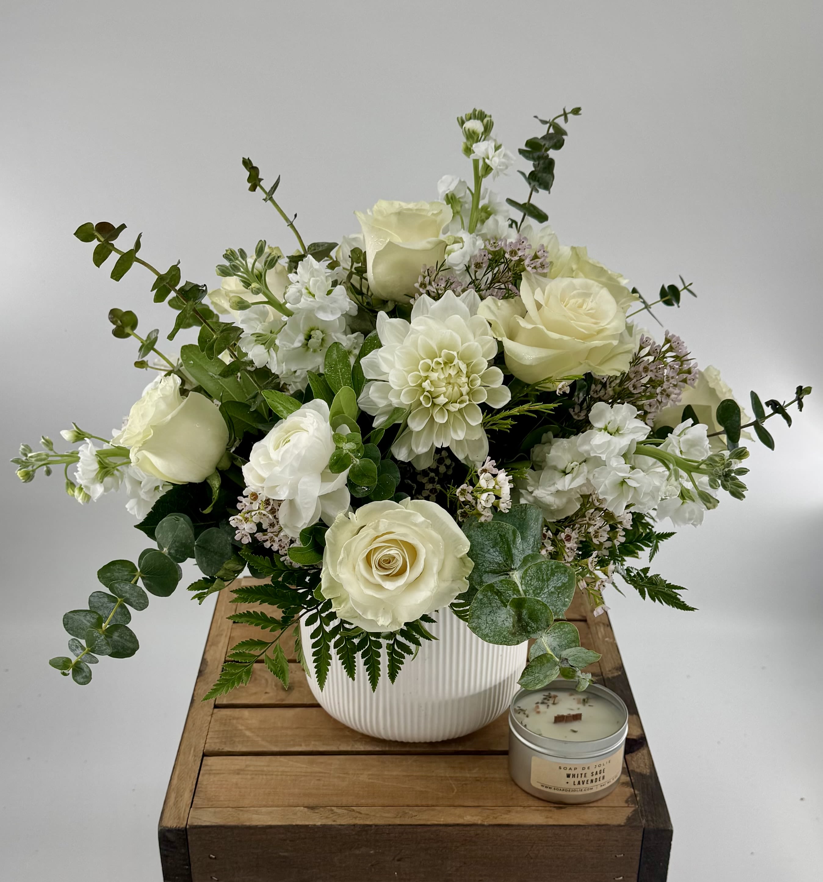 White rose arrangement in a ribbed vase with a small candle beside it